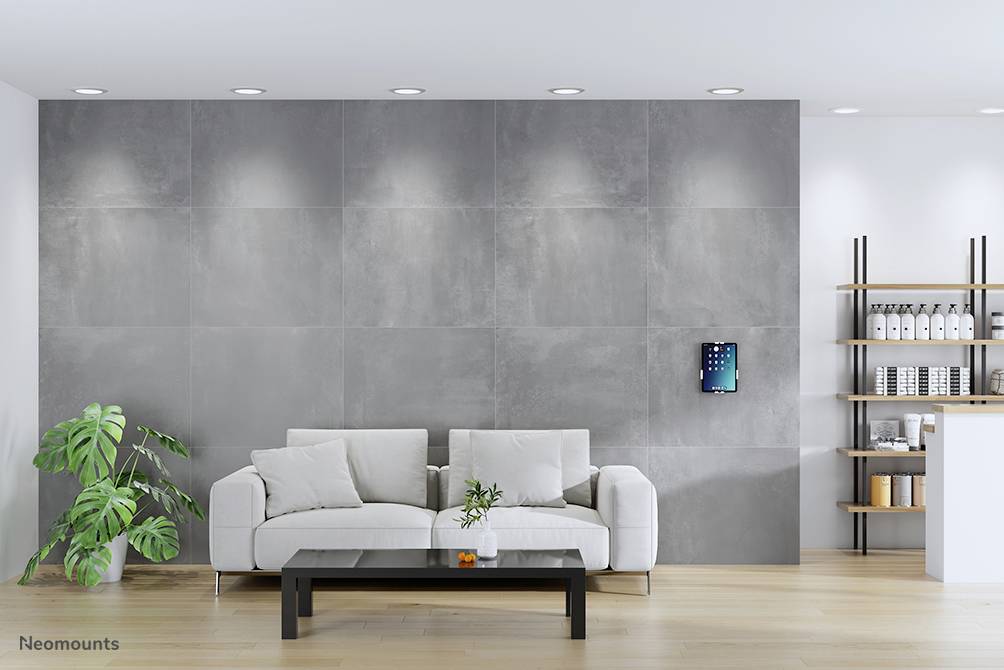 Ein modernes Wohnzimmer mit grauer Wand, weißem Sofa und Couchtisch. An der Wand hängt ein Bildschirm. Rechts stehen Regale.