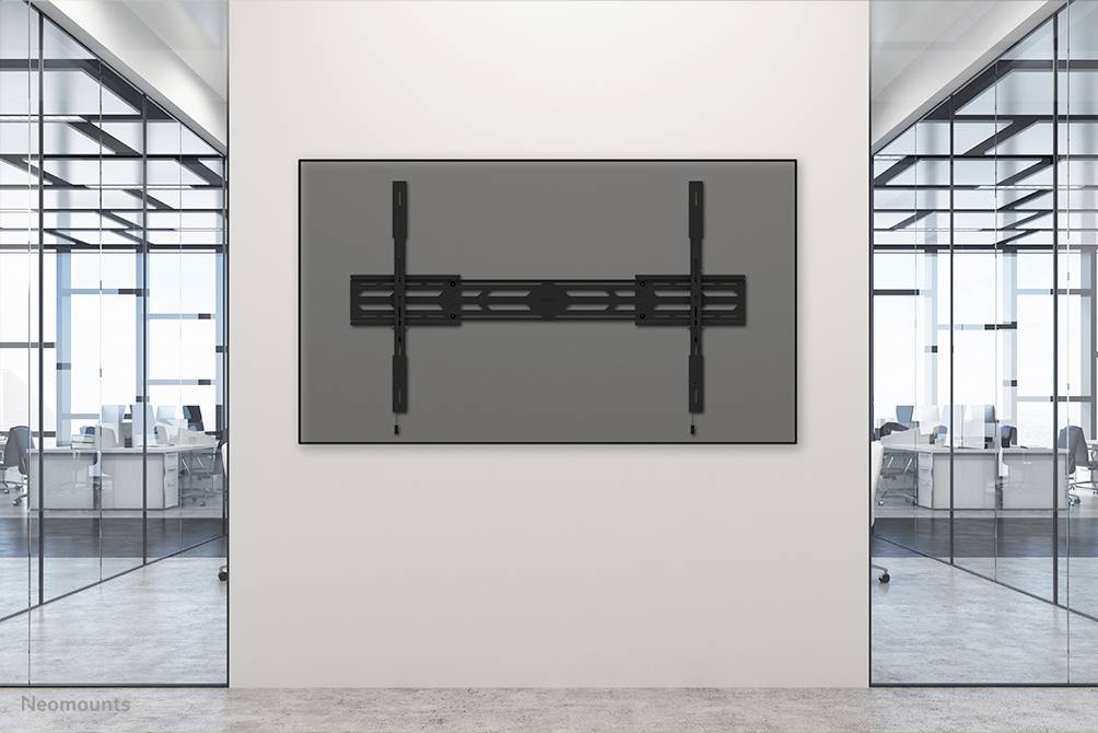 Ein Büro mit modernen Glastrennwänden und aufgeräumten Arbeitsstationen. An der Wand hängt ein großer schwarzer Bildschirm.