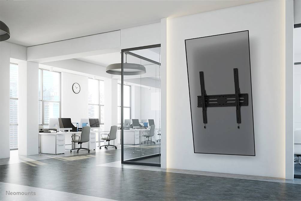 Büro mit modernen Möbeln, leeren Schreibtischen und einem großen Bildschirm an der Wand, der schräg nach oben angebracht ist.
