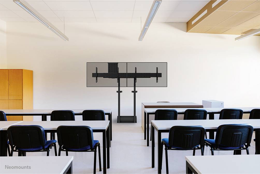 Ein Klassenzimmer mit mehreren Schreibtischen und Stühlen, im Hintergrund ein leerer Bildschirmständer ohne Monitor, neutrale Farben.
