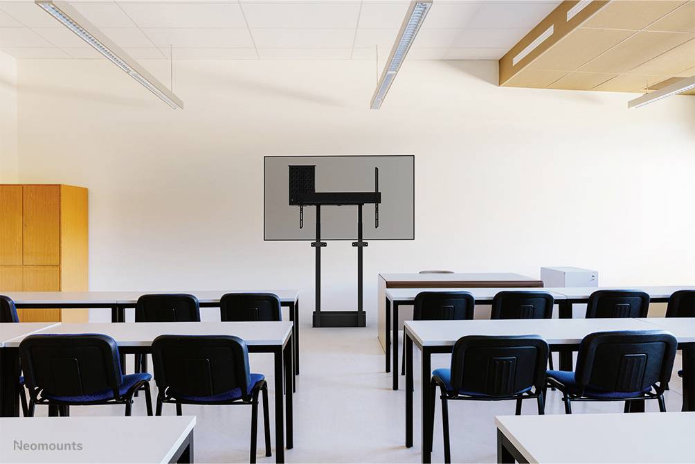 Ein leerer Seminarraum mit weißen Tischen und schwarzen Stühlen, im Hintergrund steht ein großer Bildschirm auf einem Gestell.