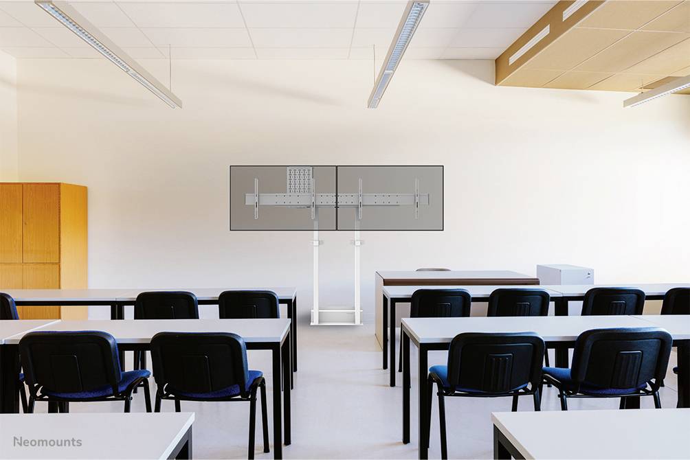 Ein leerer Klassenraum mit Tischen und Stühlen. Vorne steht ein großer Monitor auf einem Standfuß. Die Umgebung ist hell beleuchtet.