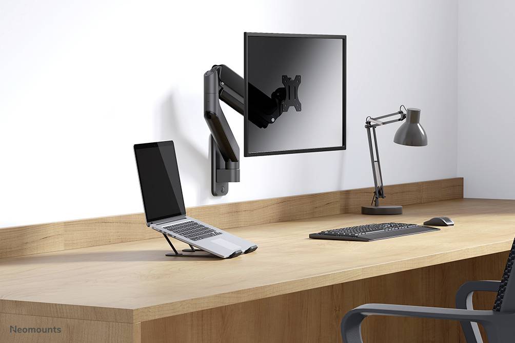 Ein Schreibtisch mit einem Laptopständer, Laptop, Halter für einen Monitor, Monitor darüber, eine Tastatur und eine Schreibtischlampe.