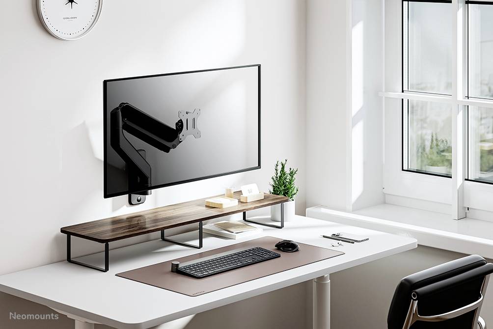 Ein minimalistischer Arbeitsplatz mit einem an der Wand montierten Monitor, einer Tastatur und einer Maus auf einem weißen Tisch neben einem Fenster.