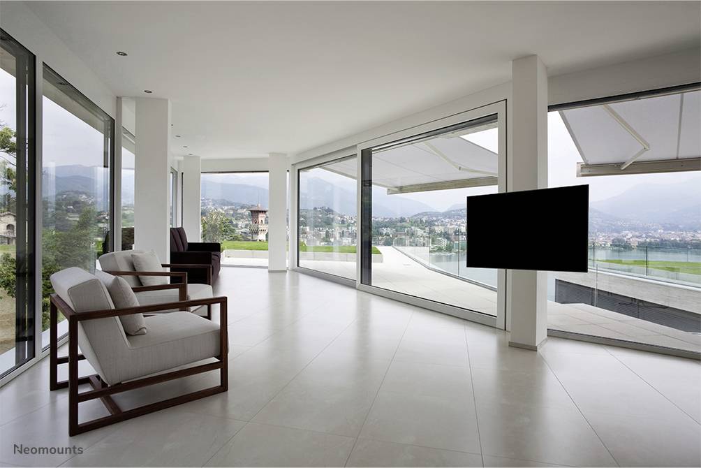 Ein moderner, leerer Wohnraum mit großen Fenstern und Blick auf eine weitläufige Landschaft. Rechts ist ein schwarzer Fernseher an der Wand montiert.