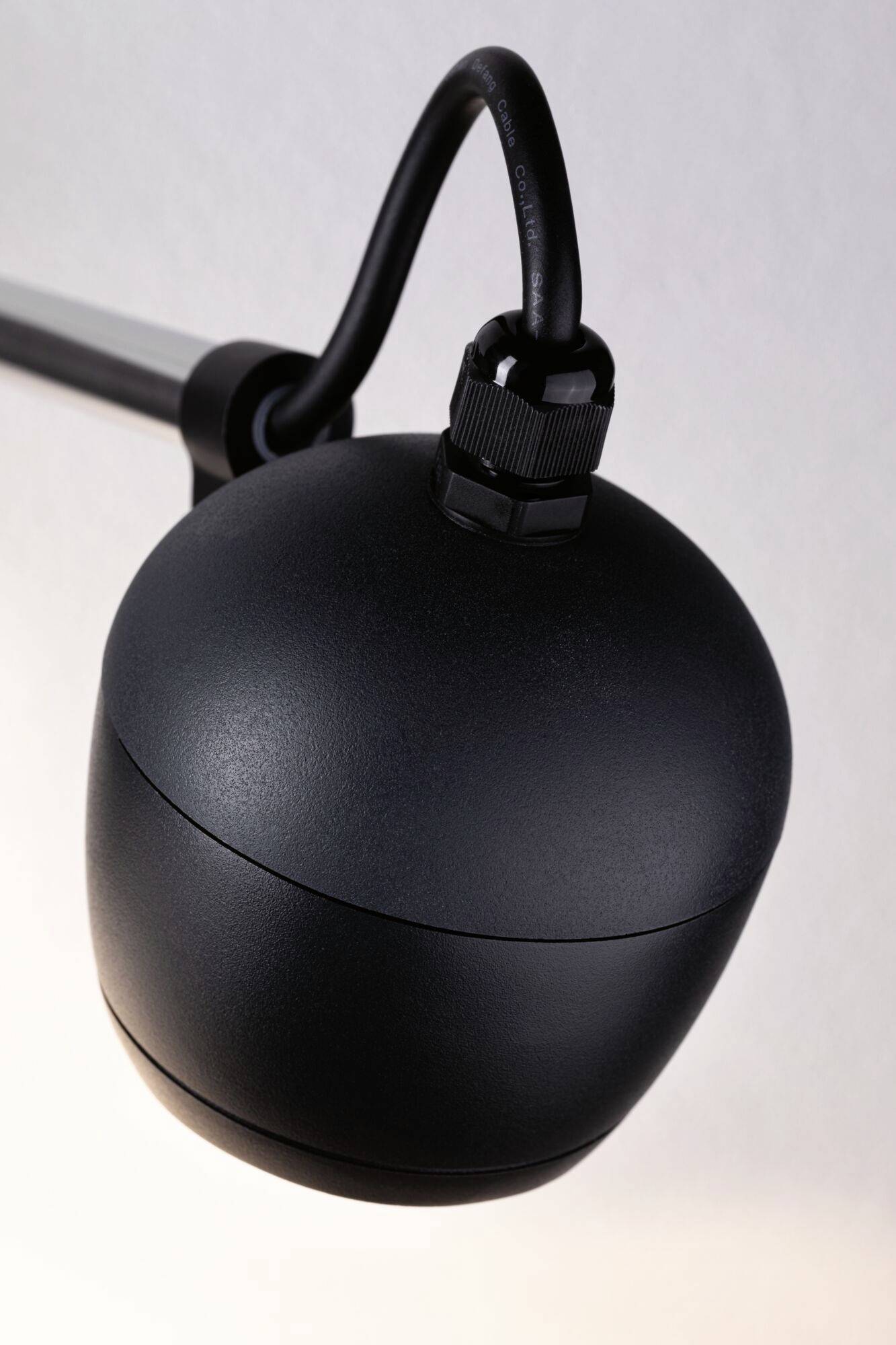 Eine schwarze, kugelförmige Lampe mit Kabel hängt an einer Metallstange.