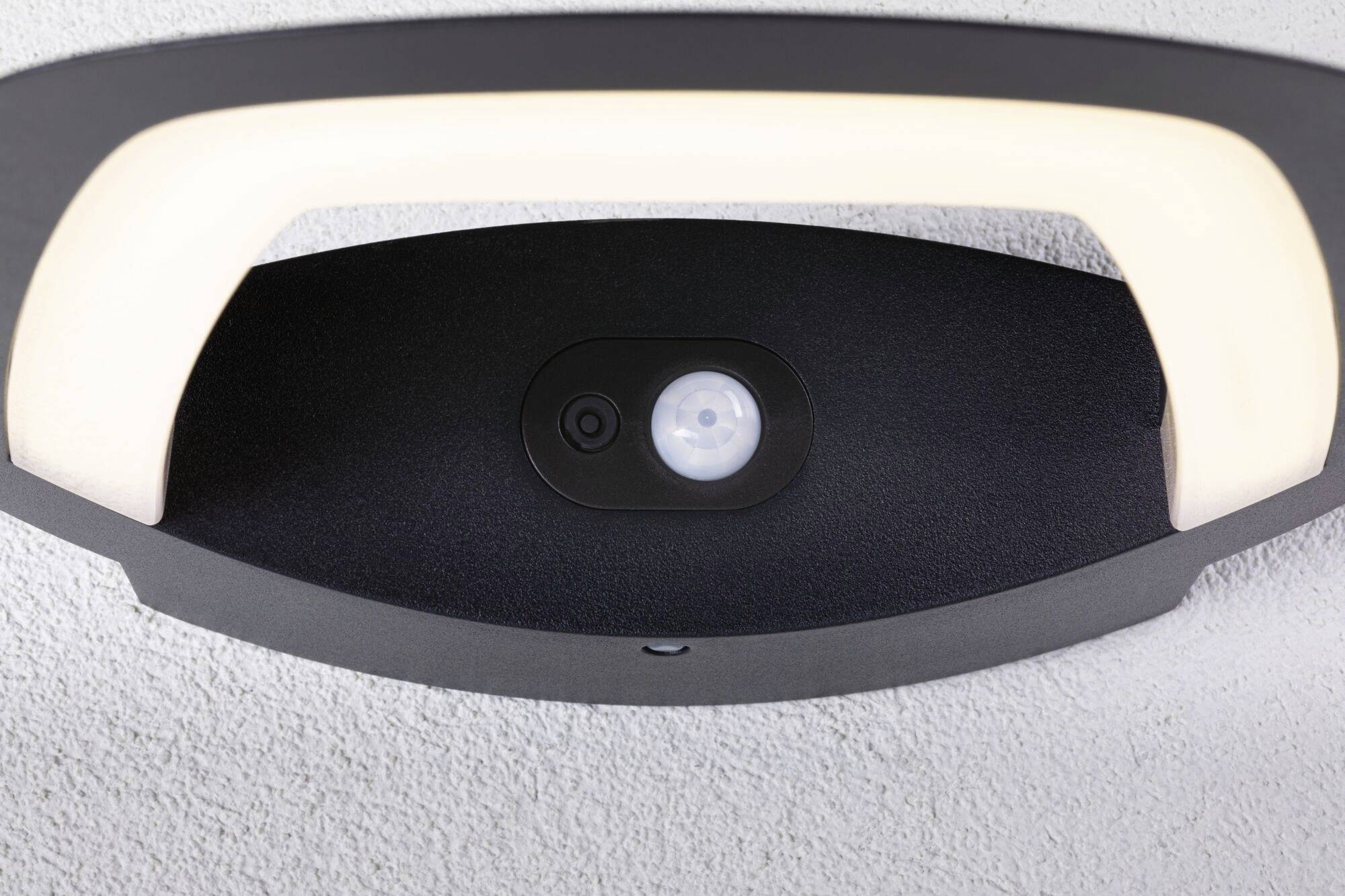 Deckenlampe mit integriertem Sensor für Bewegungsmelder an einer weißen Decke, modernes Design mit ovaler Form und schwarzer Umrandung.