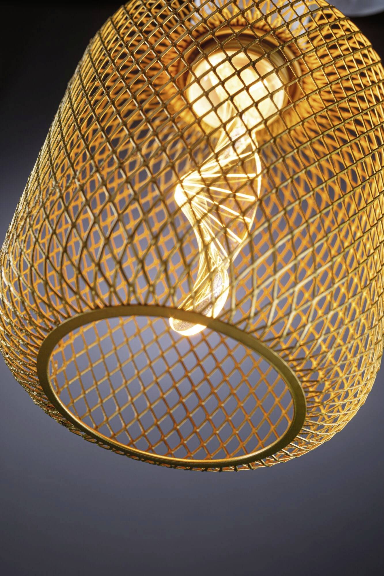 Eine gelbe, geflochtene Lampe mit Glühbirne, die warmes Licht abstrahlt, vor dunklem Hintergrund.