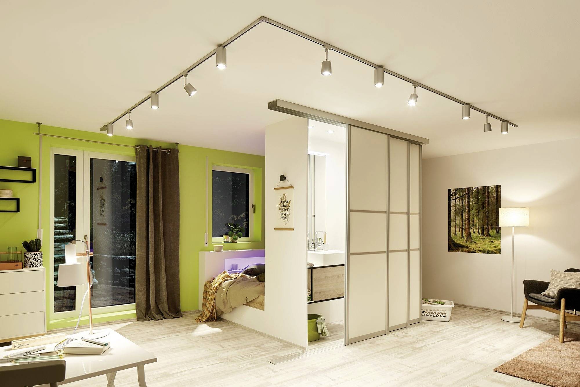 Ein modernes Wohnzimmer mit grüner Wand, Schiebetür zu einem Schlafzimmer, mehreren Deckenstrahlern und einem großen Fenster.