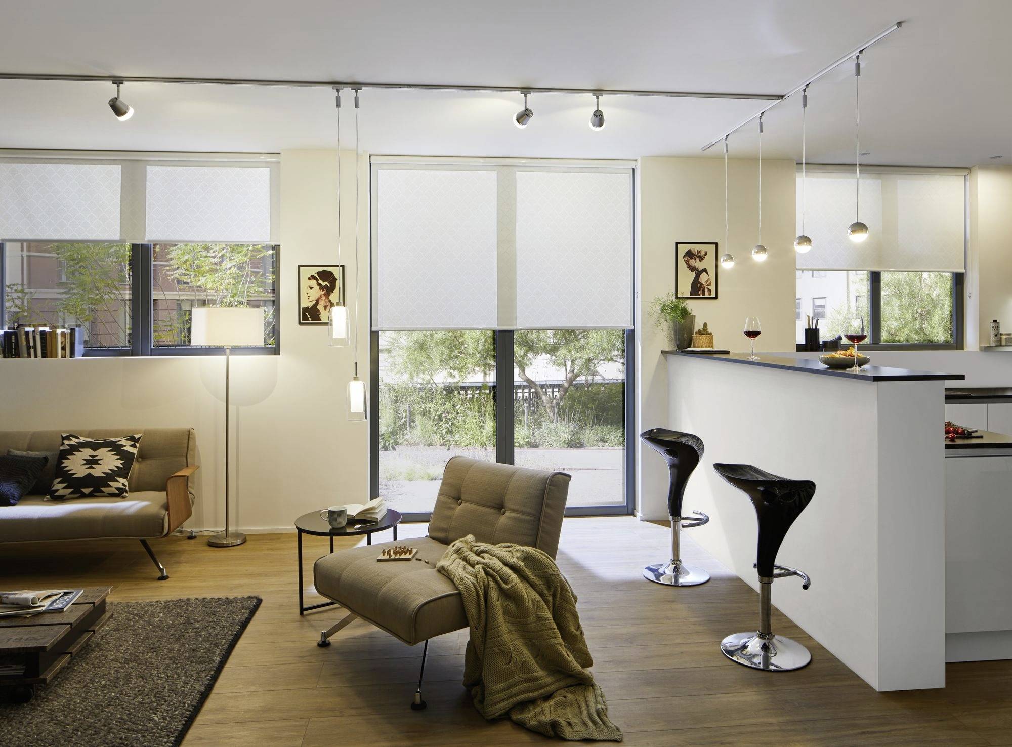 Ein modern eingerichtetes Wohnzimmer mit großen Fenstern, zwei Barhockern an einer Theke, einem Sofa und einem Sessel.