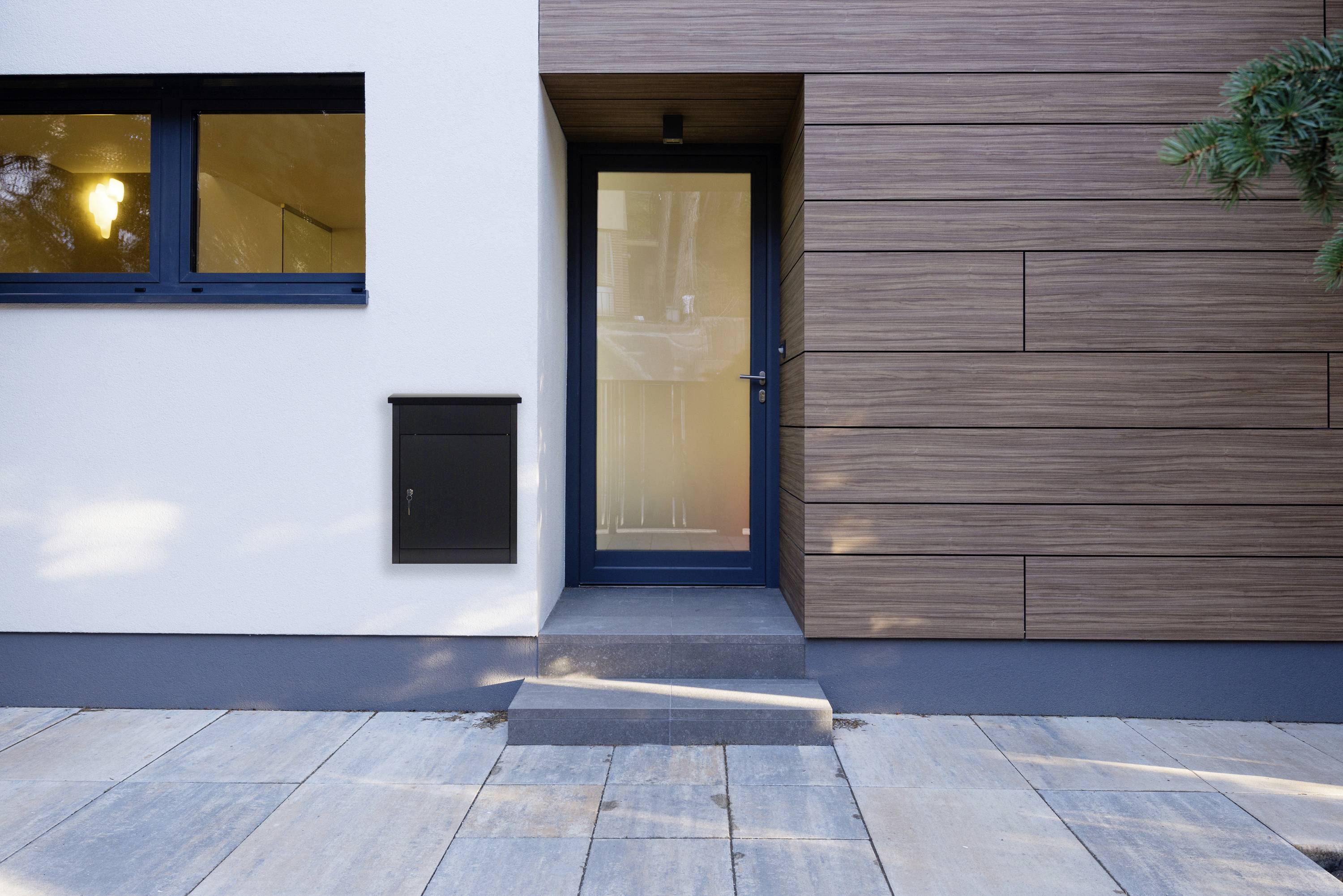 Eingangstür eines modernen Hauses, umgeben von Holz- und Putzfassaden, mit einem Fenster links und einem kleinen Briefkasten.