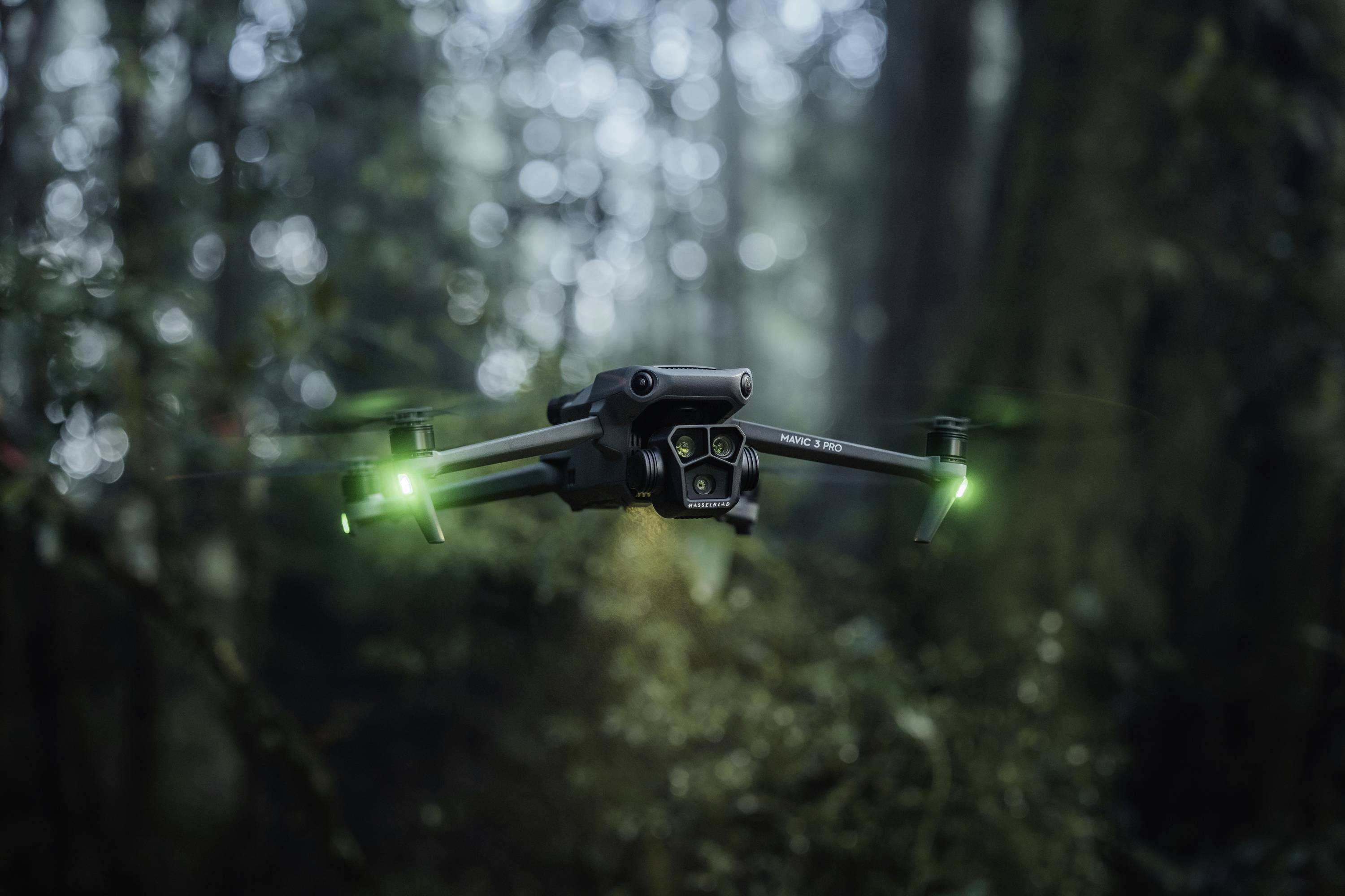 Drohne mit leuchtenden grünen Lichtern schwebt in einem nebligen Wald, umgeben von unscharfen Bäumen.