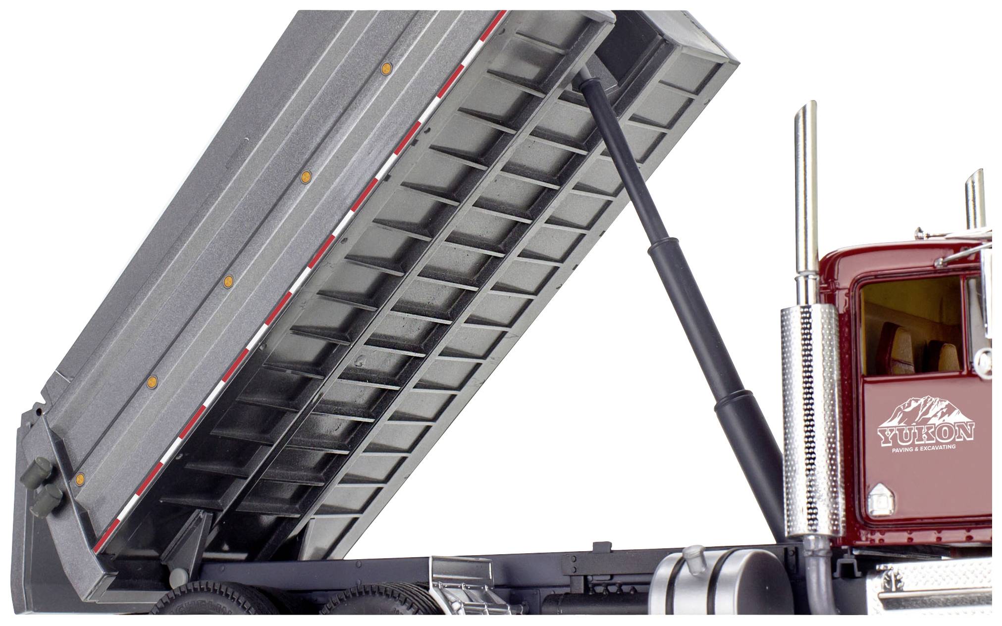 Kipp-Lkw von der Seite. Die Ladefläche ist angehoben, zeigt Stabilitätsstruktur. Rot lackierte Fahrerkabine mit Yukon-Logo.