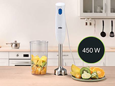 Ein weißer Stabmixer mit einem 450-Watt-Motor steht neben einem Mixbecher mit Obststücken in einer Küchenumgebung.