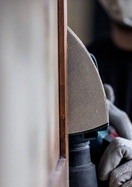 Eine Person schleift mit einer elektrischen Schleifmaschine eine Holzoberfläche. Sie trägt graue Schutzhandschuhe zur Sicherheit.