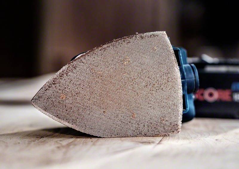 Ein Schleifgerät liegt auf der Seite auf einer Holzoberfläche. Der Schleifkopf zeigt nach vorne.