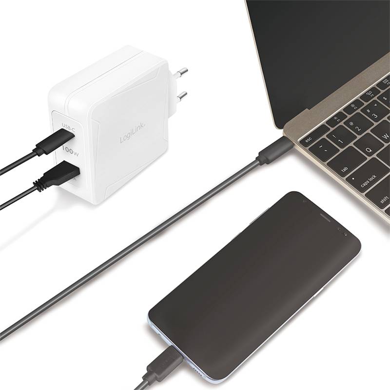 Ein Smartphone wird über ein schwarzes Kabel an einen weißen Wandadapter angeschlossen. Daneben liegt ein geöffneter Laptop.