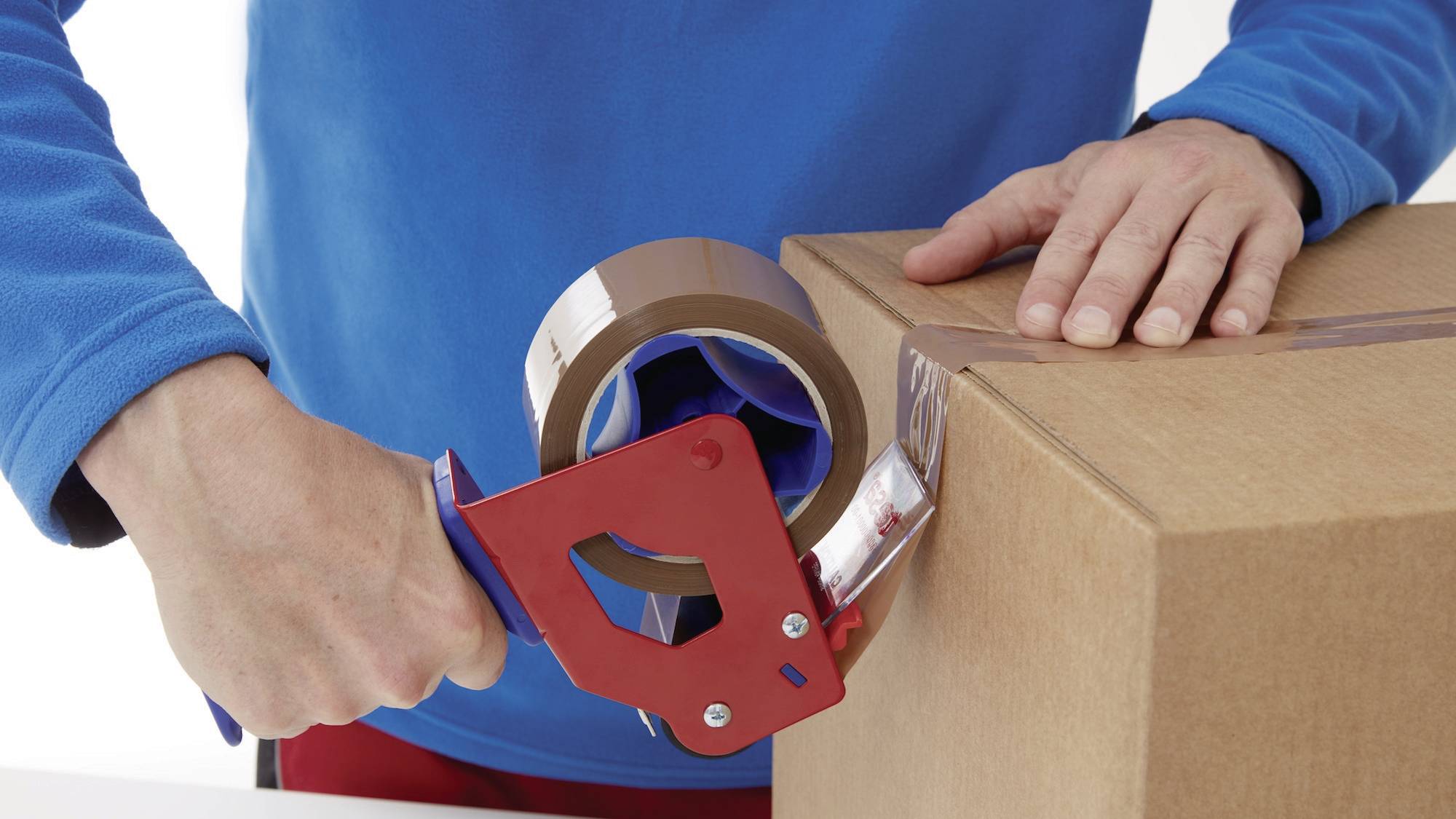 Eine Person verschließt einen Karton mit einem Klebebandabroller. Der Karton steht auf einer Arbeitsfläche.