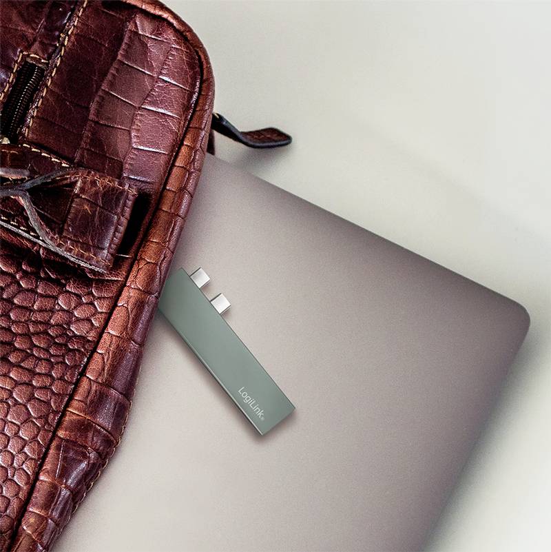 Ein rotes Lederetui liegt auf einem silbernen Laptop, in den ein USB-Stick eingesteckt ist.