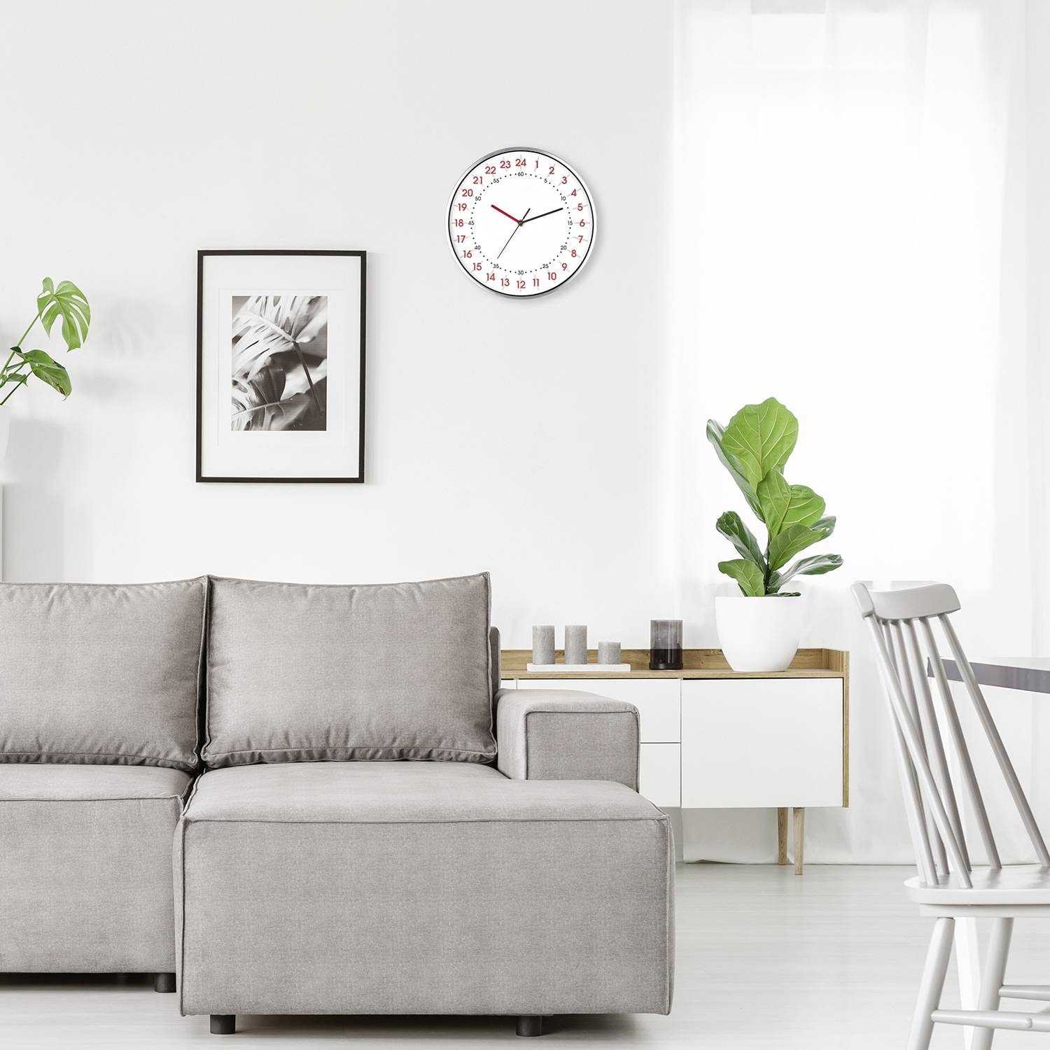 Helles Wohnzimmer mit grauem Sofa, Uhr an der Wand zeigt 10:10 Uhr, Pflanzen und Bild als Dekoration, ruhige und moderne Atmosphäre.