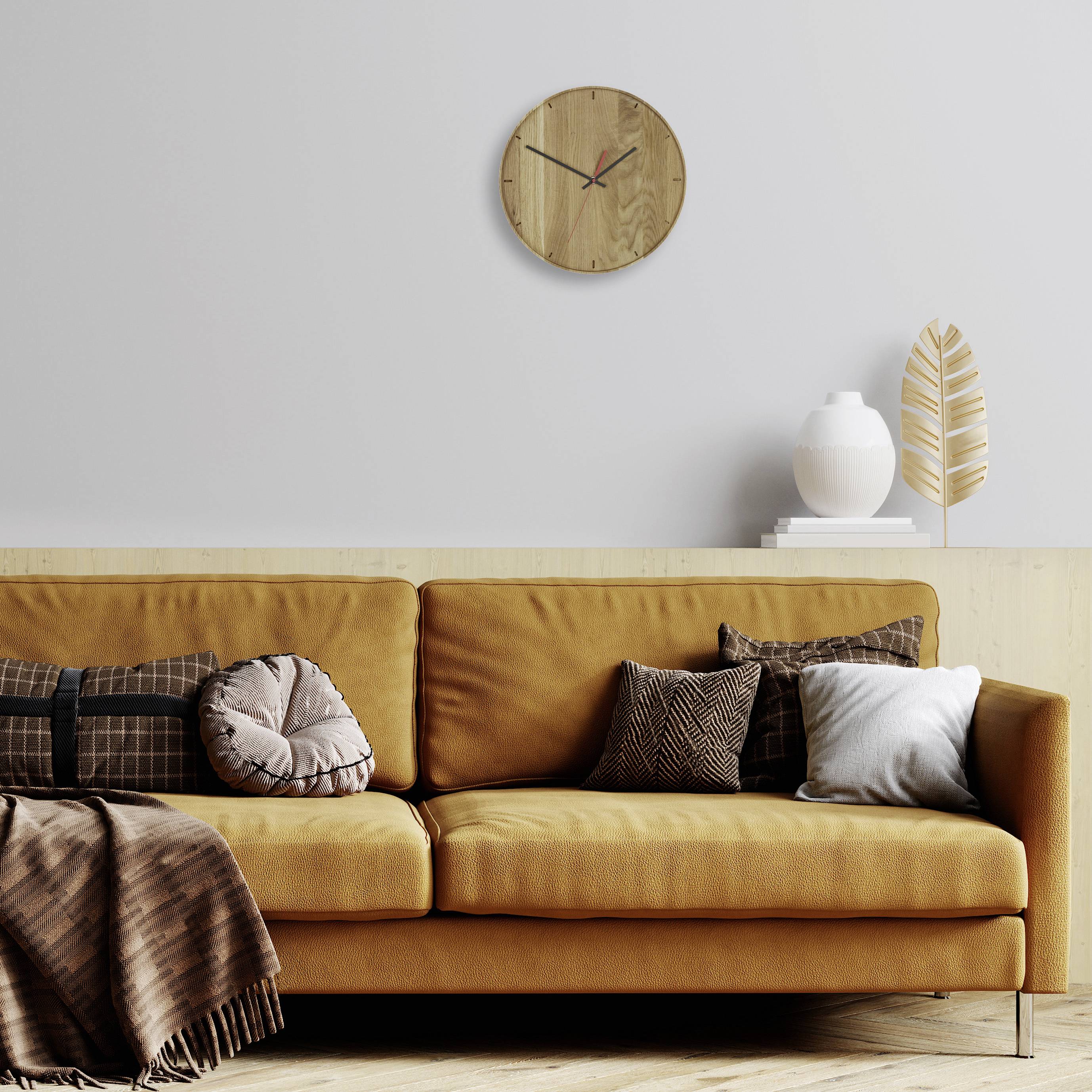 Ein modernes Wohnzimmer mit braunem Sofa, Kissen, einer braunen Decke. An der Wand hängt eine runde Holzuhr; daneben eine Pflanze.