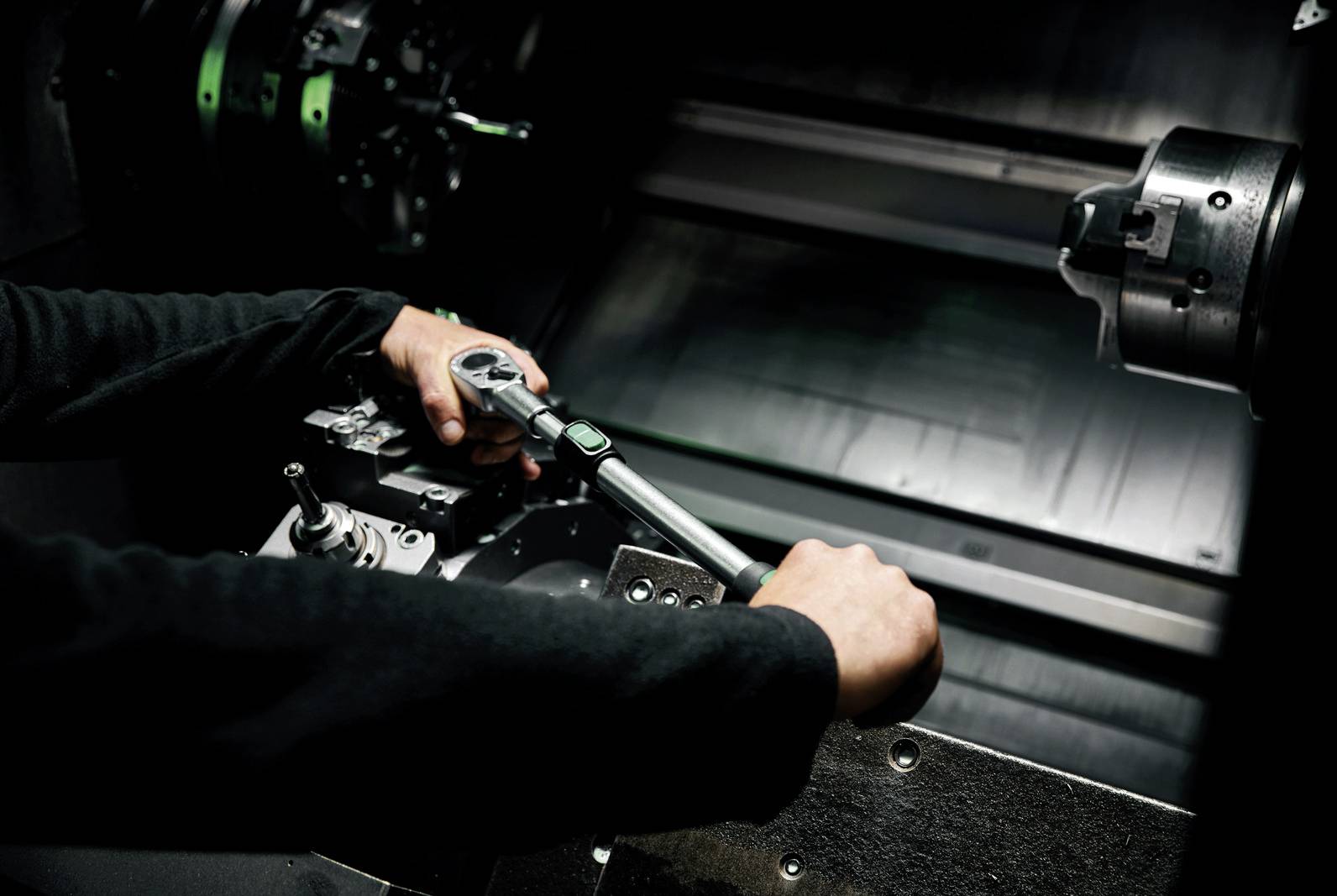 Eine Person arbeitet an einer CNC-Maschine in einem dunklen Raum. Sie hält ein Werkzeug und justiert vorsichtig eine Metallkomponente.