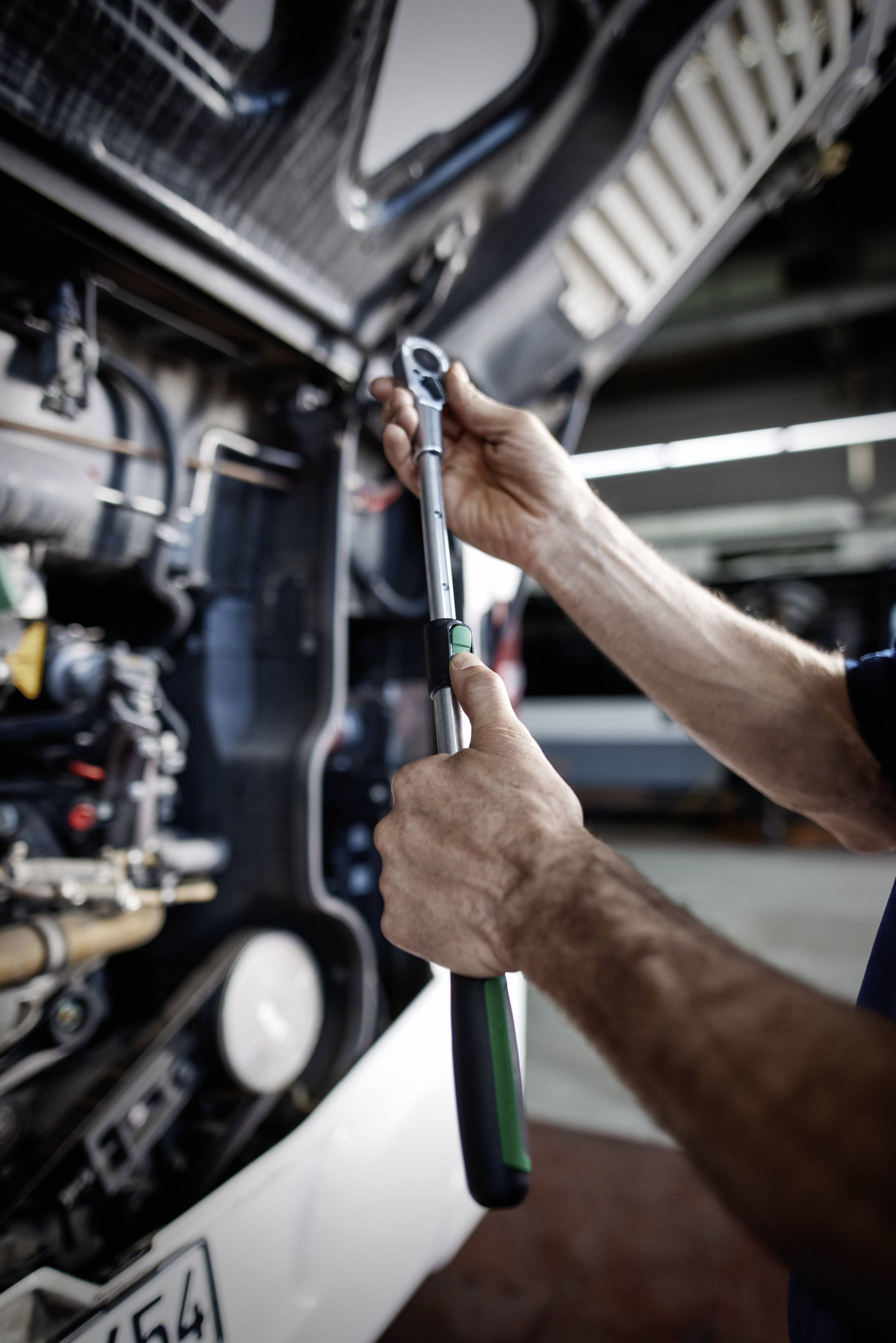 Eine Person justiert einen großen Schraubenschlüssel an einem Truck-Motor und konzentriert sich auf einen bestimmten Teil. Das Bild betont mechanische Reparaturarbeiten.