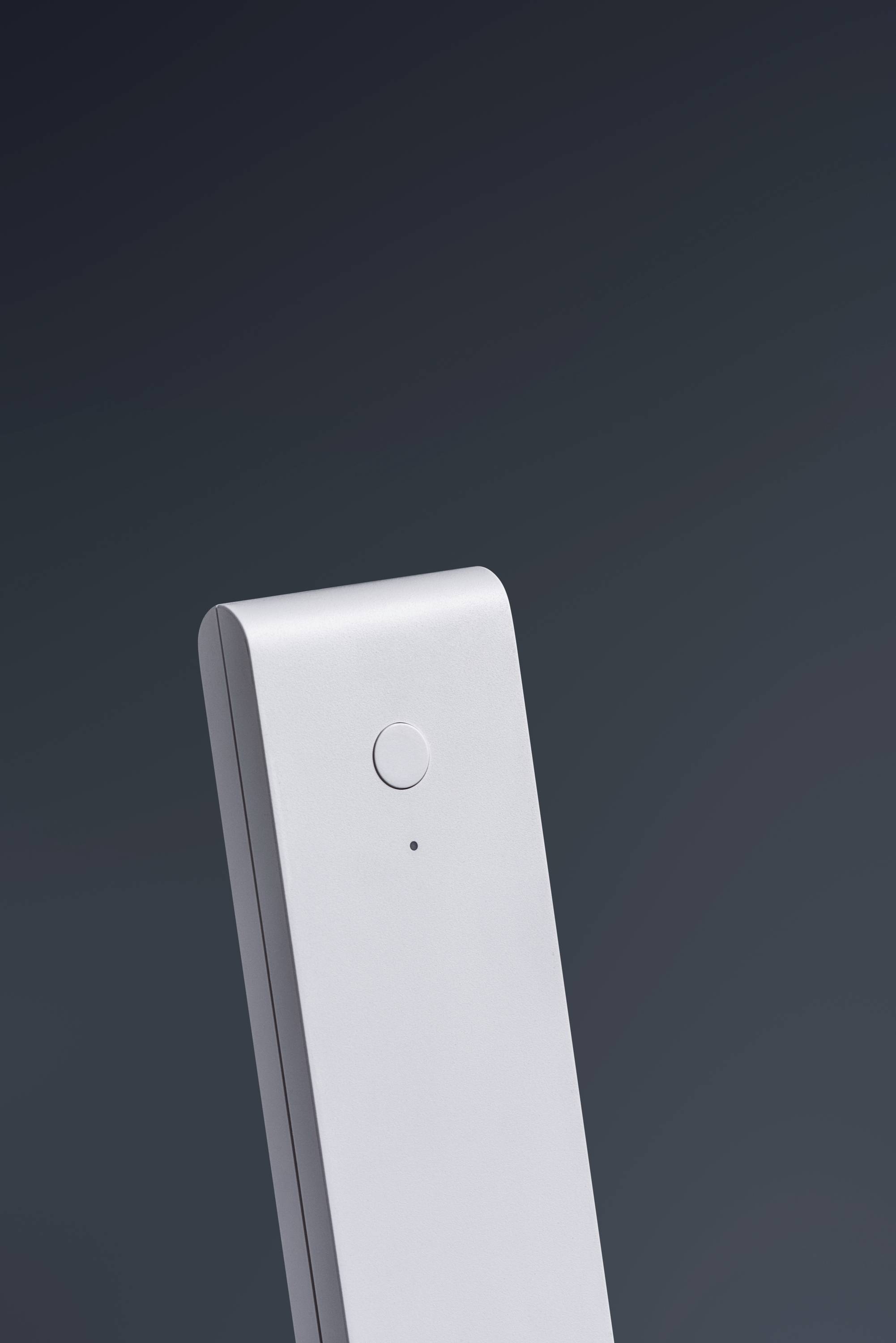 Ein schlichtes, modernes Gerät mit einem Knopf und einer LED-Anzeige, vor einem dunklen Hintergrund, möglicherweise ein Fernbedienungsteil.