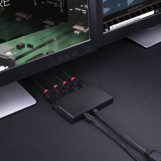 Ein schwarzer HDMI-Splitter verbindet zwei Monitore mit mehreren HDMI-Kabeln auf einem Tisch.