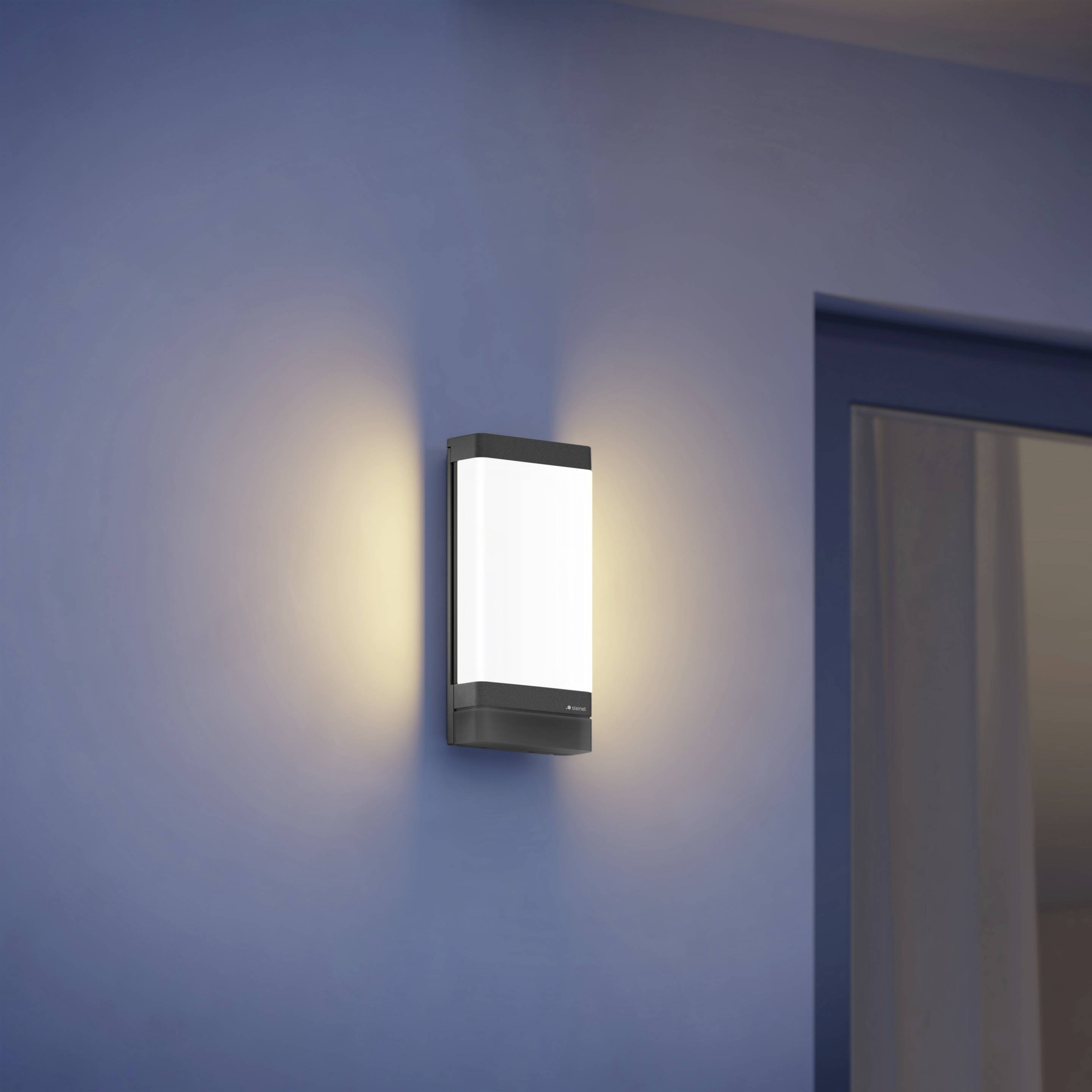 Moderne Wandleuchte mit rechteckigem Design strahlt warmes Licht auf eine blaue Wand.