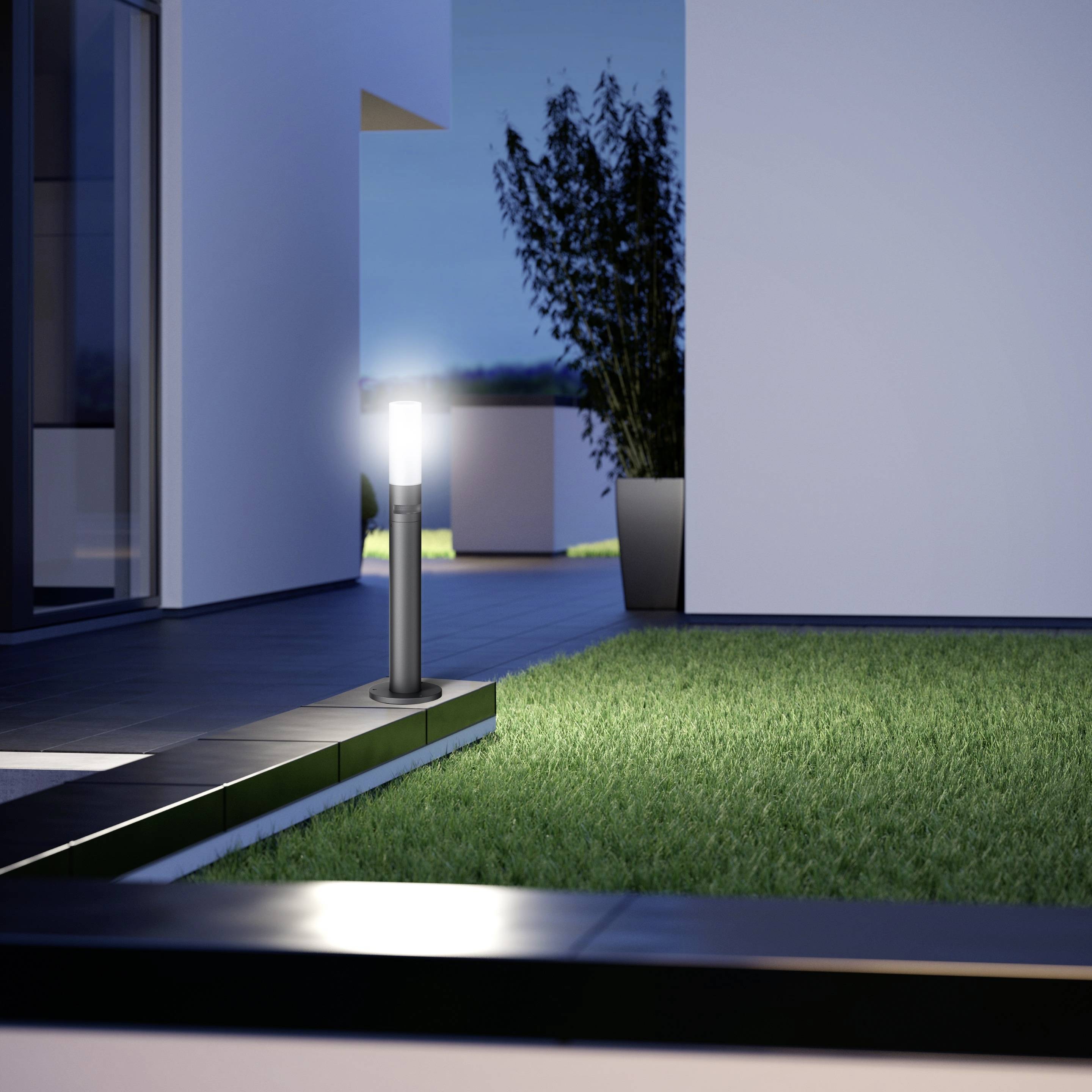 Ein Gartenweg bei Dämmerung zeigt moderne Außenbeleuchtung in Form von kleinen, leuchtenden Lampen entlang eines grünen Rasens.