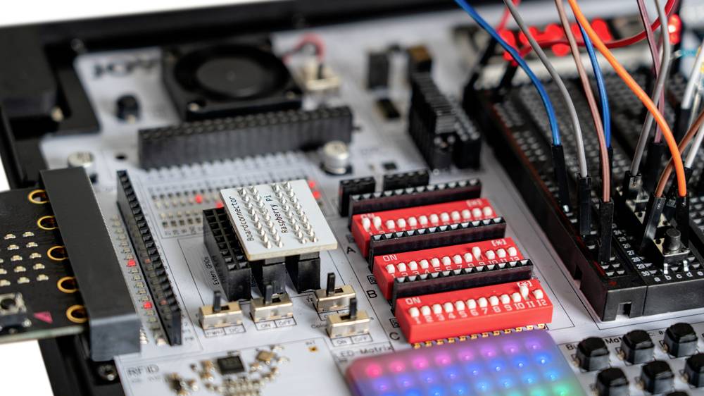 Nahaufnahme einer elektronischen Platine mit mehreren Chips, Steckverbindungen und farbigen Kabeln. Entwicklermodul in einem technischen Kontext.