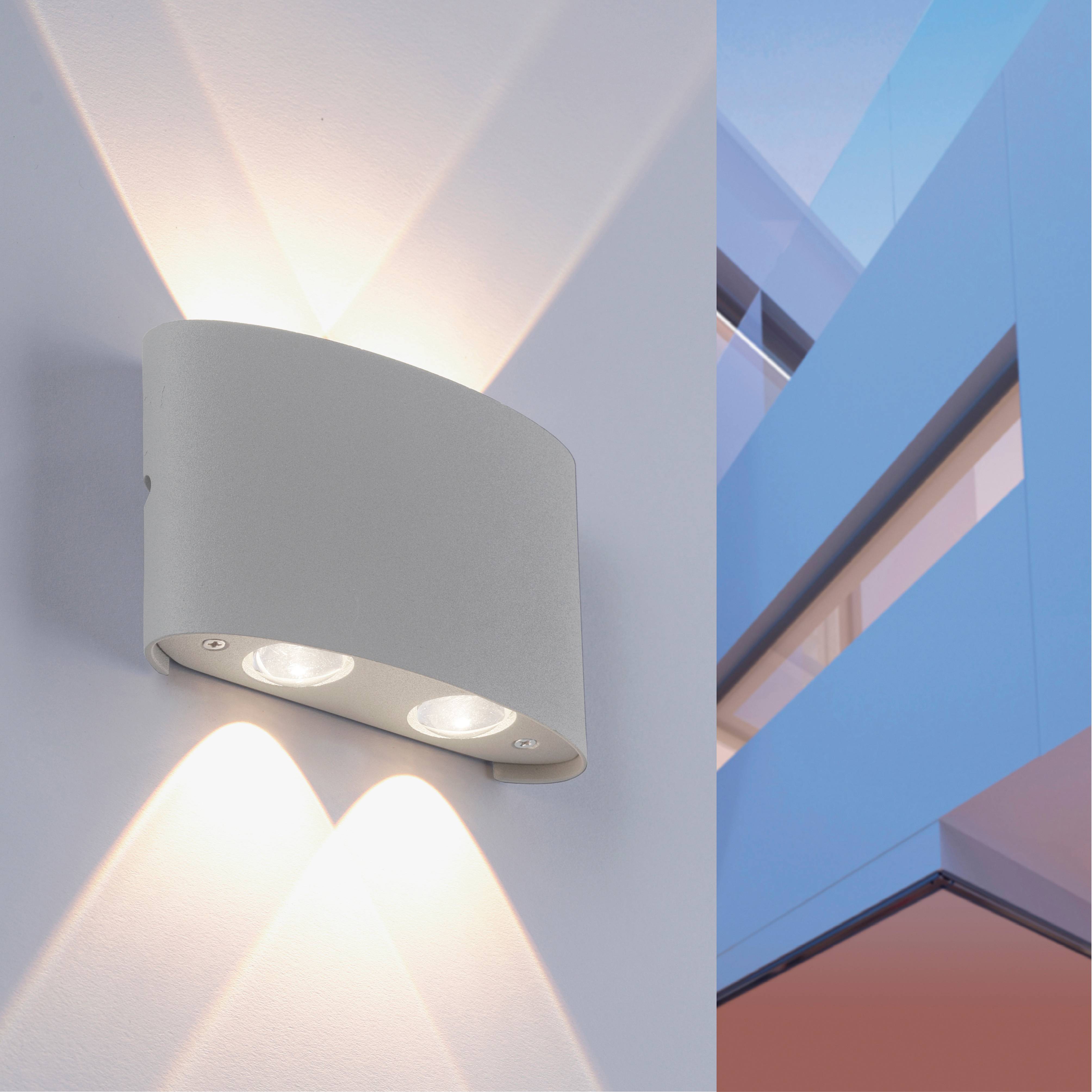Wandleuchte mit modernem Design an einer weißen Wand, beleuchtet nach oben und unten. Rechte Seite zeigt einen blauen und weißen Gebäudeteil.