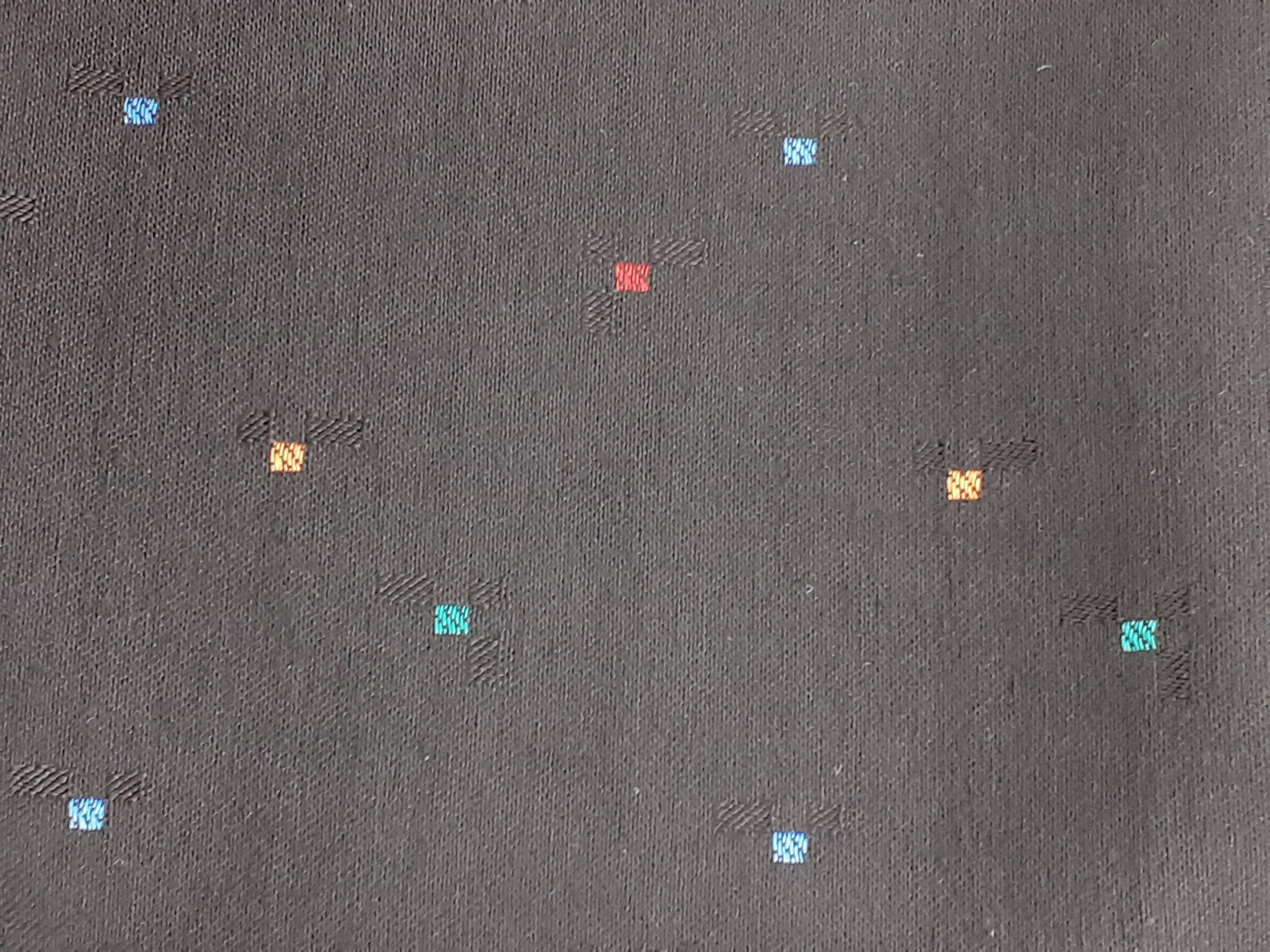 Dunkler Stoff mit vereinzelten kleinen Vierecken in Blau, Rot und Gelb.