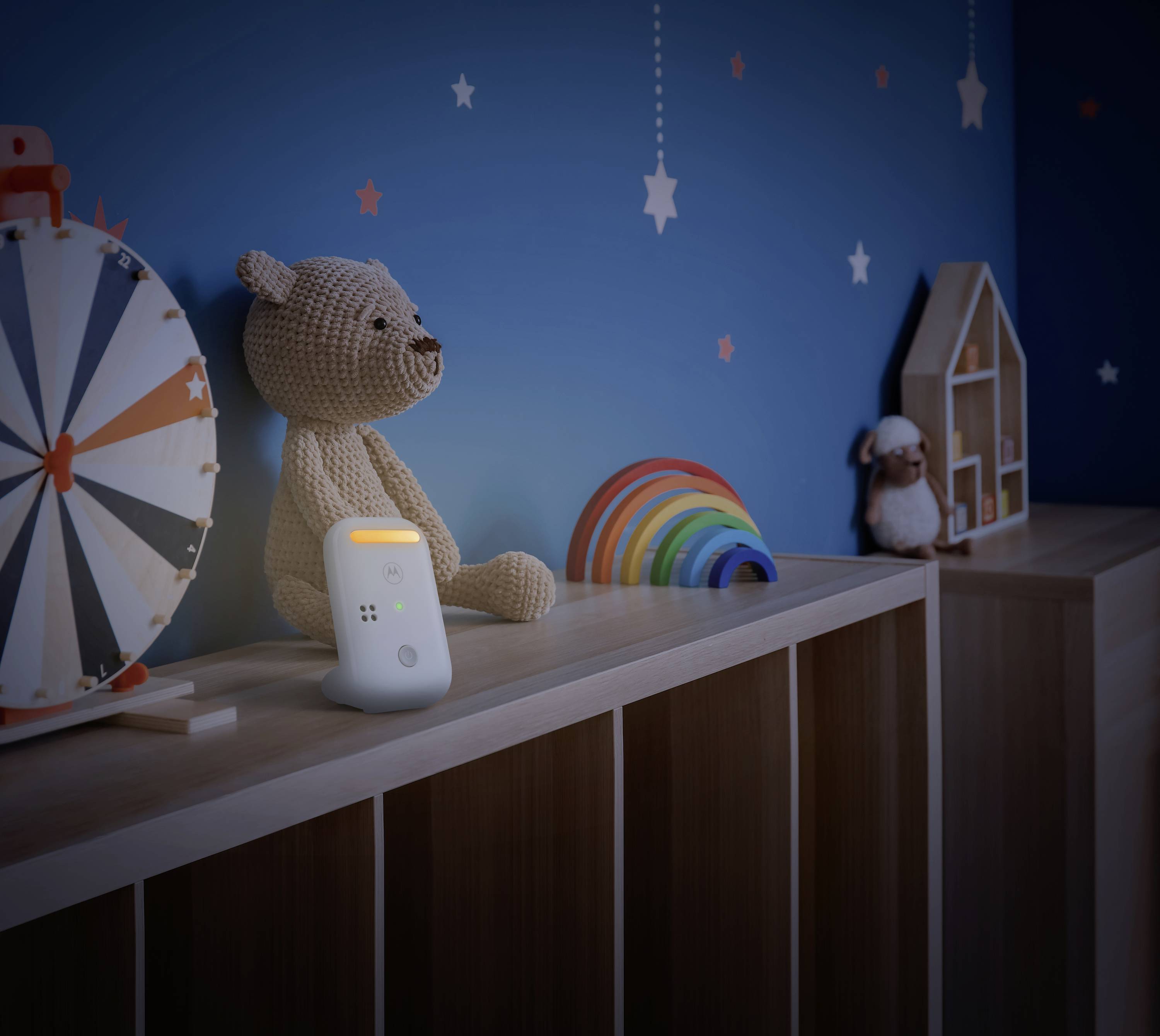 Ein Kinderzimmer mit einem Spielzeugbär und einer Nachtlichtlampe auf einem Regal. Der blaue Hintergrund hat Sterne als Dekoration.