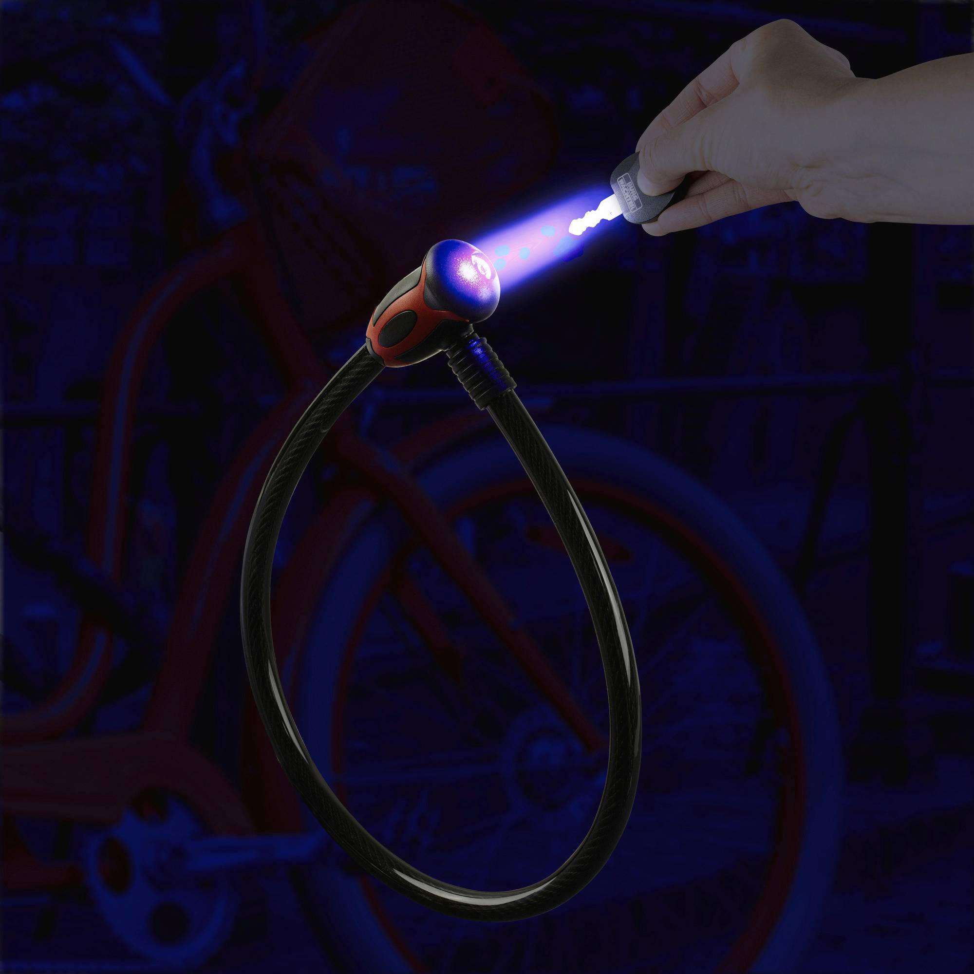 Ein Hand drückt einen leuchtenden Knopf an einem Fahrradschloss, das im Dunkeln erstrahlt. Im Hintergrund ist ein Fahrrad zu sehen.