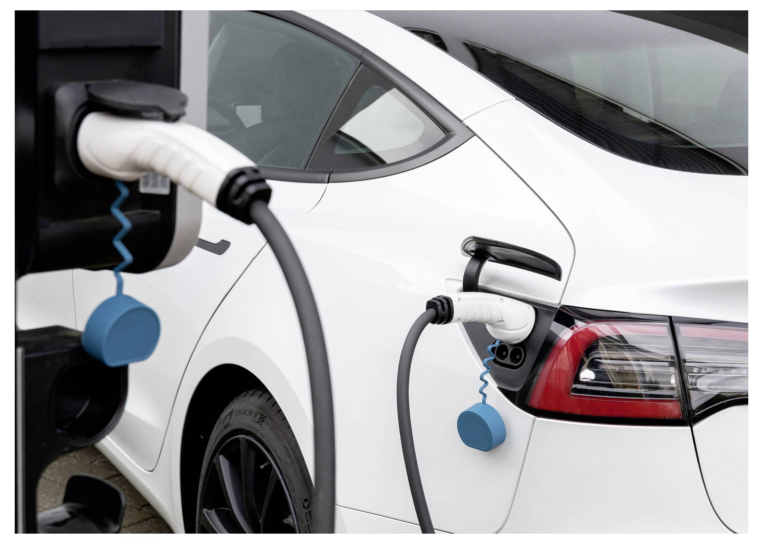 Ein weißes Auto wird mit einem Ladekabel aufgeladen. Das Ladekabel ist an einer Ladestation angeschlossen.