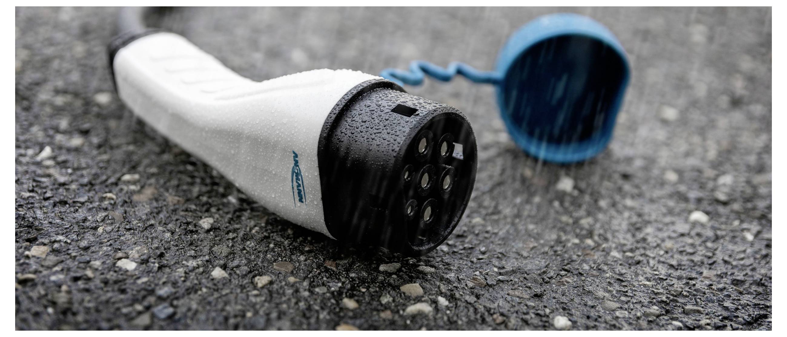 Ein nasser Ladestecker für Elektrofahrzeuge liegt auf nassen Asphalt. Der blaue Schutzdeckel ist abgenommen und im Hintergrund sichtbar.