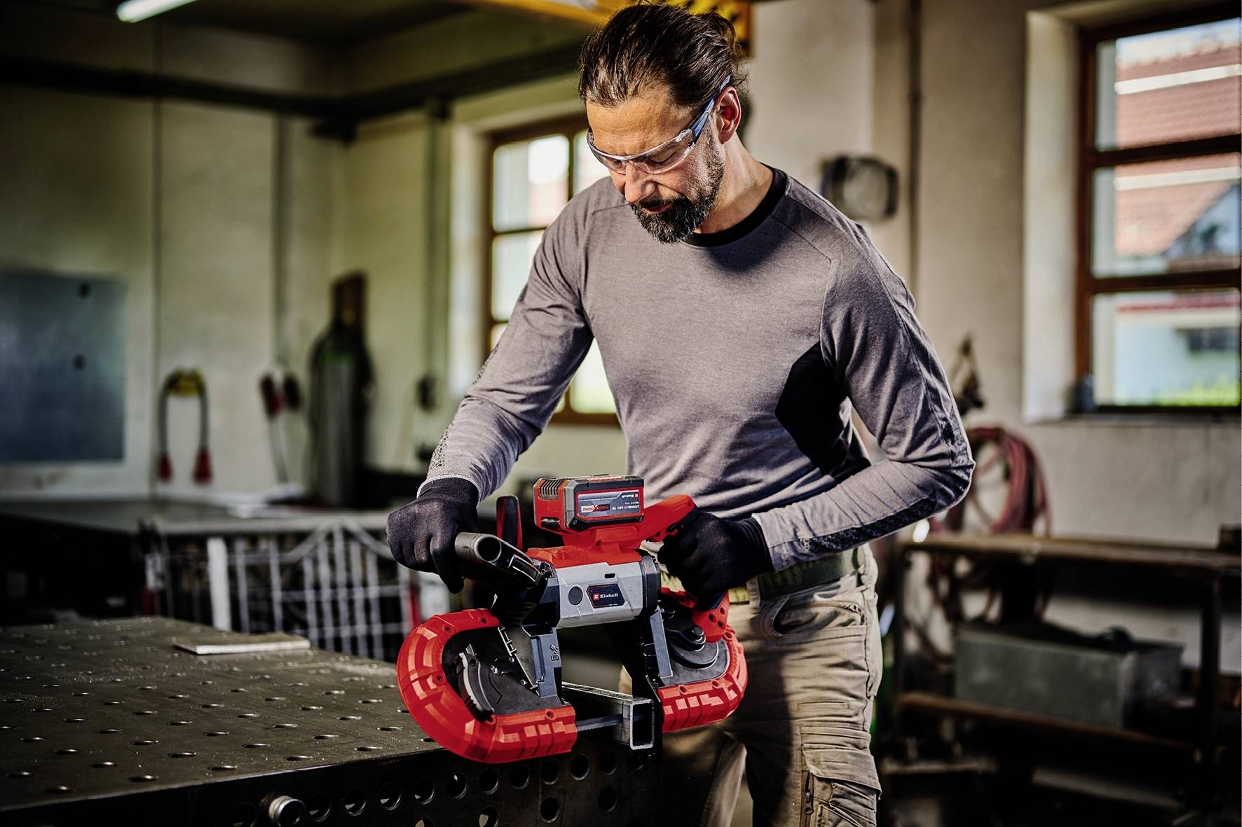 Ein Mann in Schutzbrille und Handschuhen arbeitet an einer industriell aussehenden Bandsäge in einer Werkstatt.