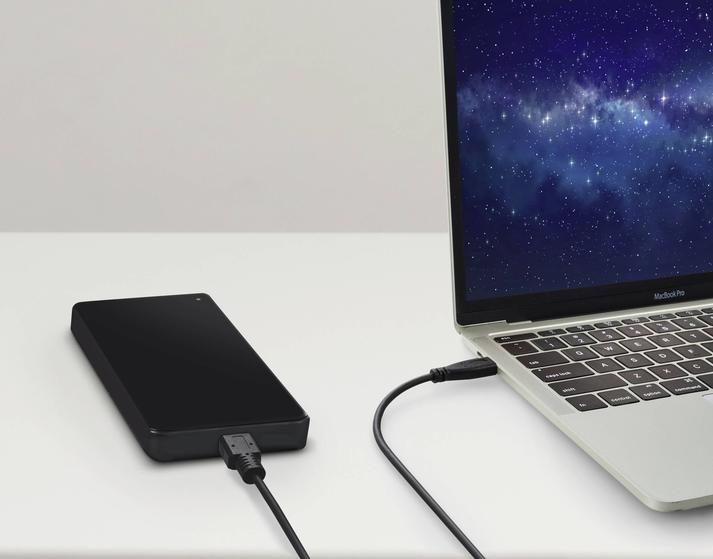 Externe Festplatte verbunden mit einem Laptop auf einem Tisch. Der Laptop zeigt einen Bildschirmhintergrund mit einem Sternenhimmel.