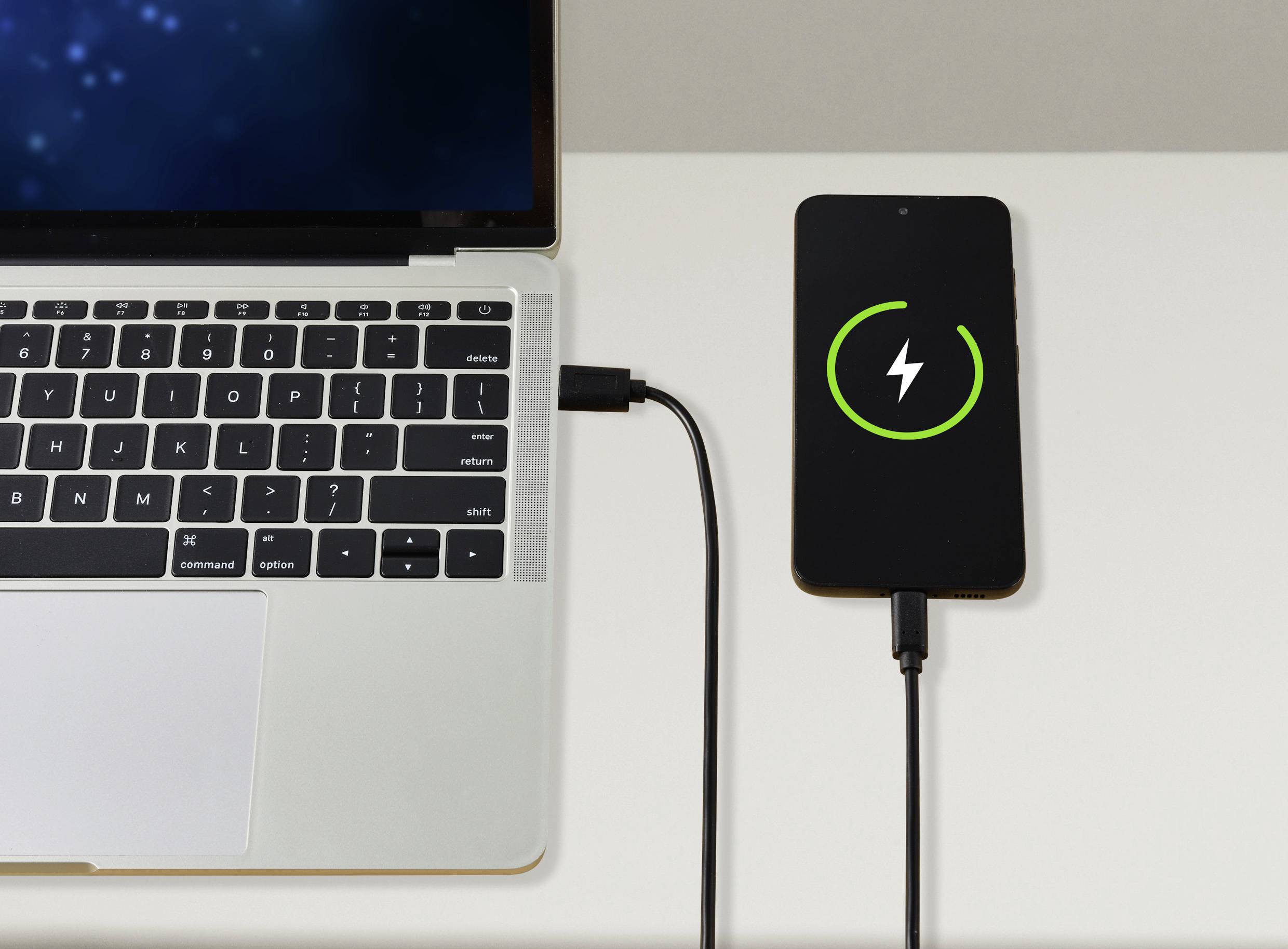 Ein Laptop ist mit einem Smartphone verbunden, das geladen wird. Das Smartphone-Display zeigt ein Ladesymbol an.