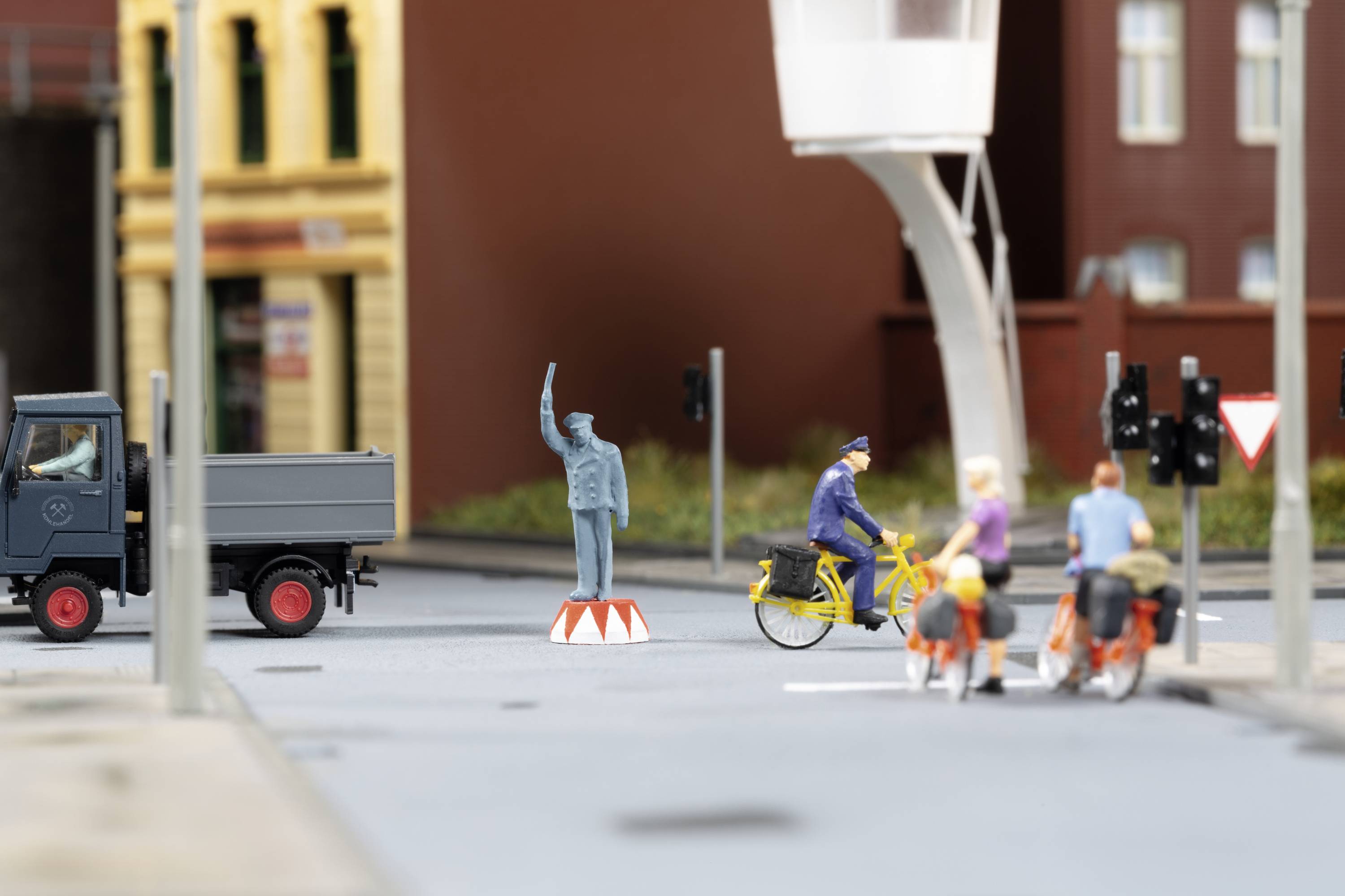 Eine Miniaturszene mit einem Lastwagen, einem Radfahrer, einem Verkehrspolizisten und einer Statue in einer städtischen Umgebung.