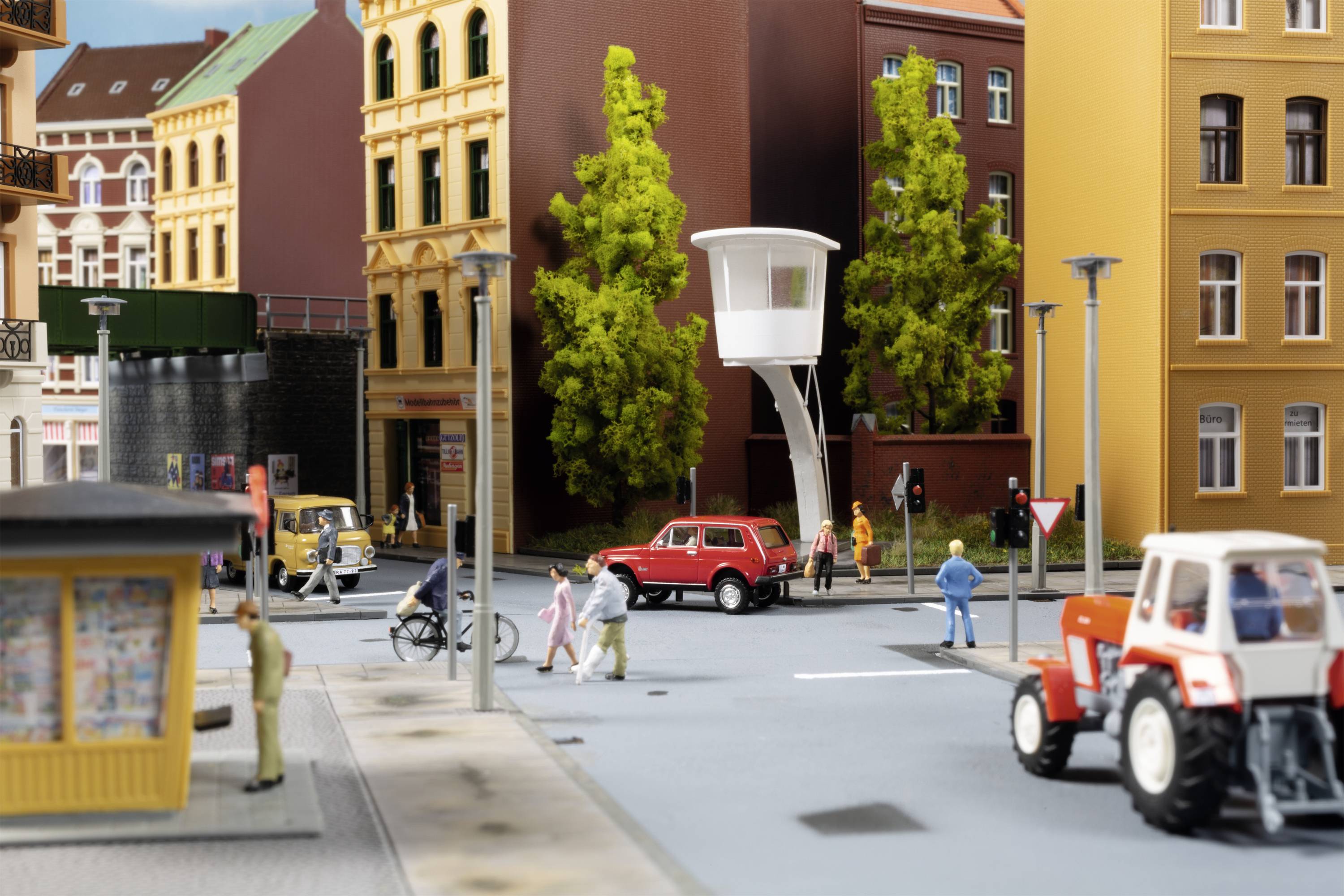 Ein detailliertes Stadtmodell mit Autos, Fahrrädern und Fußgängern an einer Kreuzung. Mehrstöckige Gebäude und Bäume im Hintergrund.