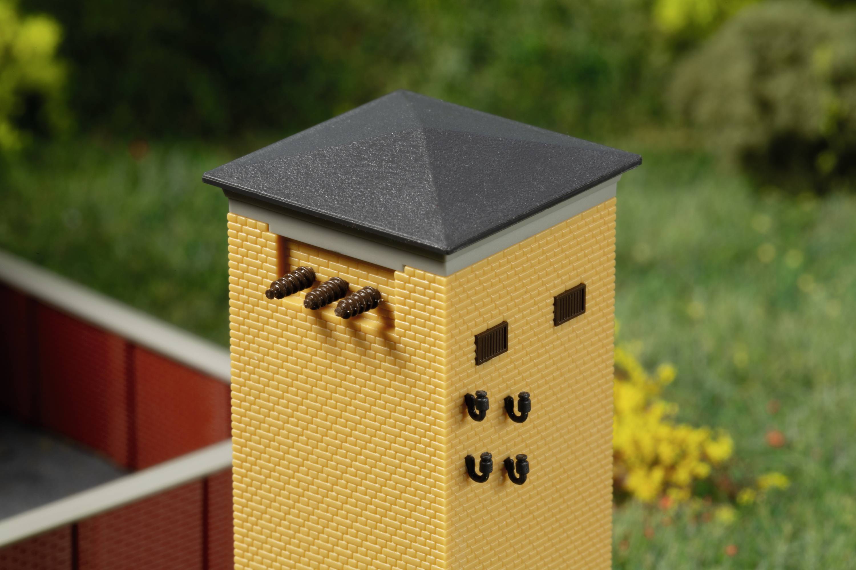 Ein gelbes Gebäude mit einem dunklen Dach und mehreren kleinen Öffnungen an der Seite, umgeben von einer grünen Landschaft im Hintergrund.