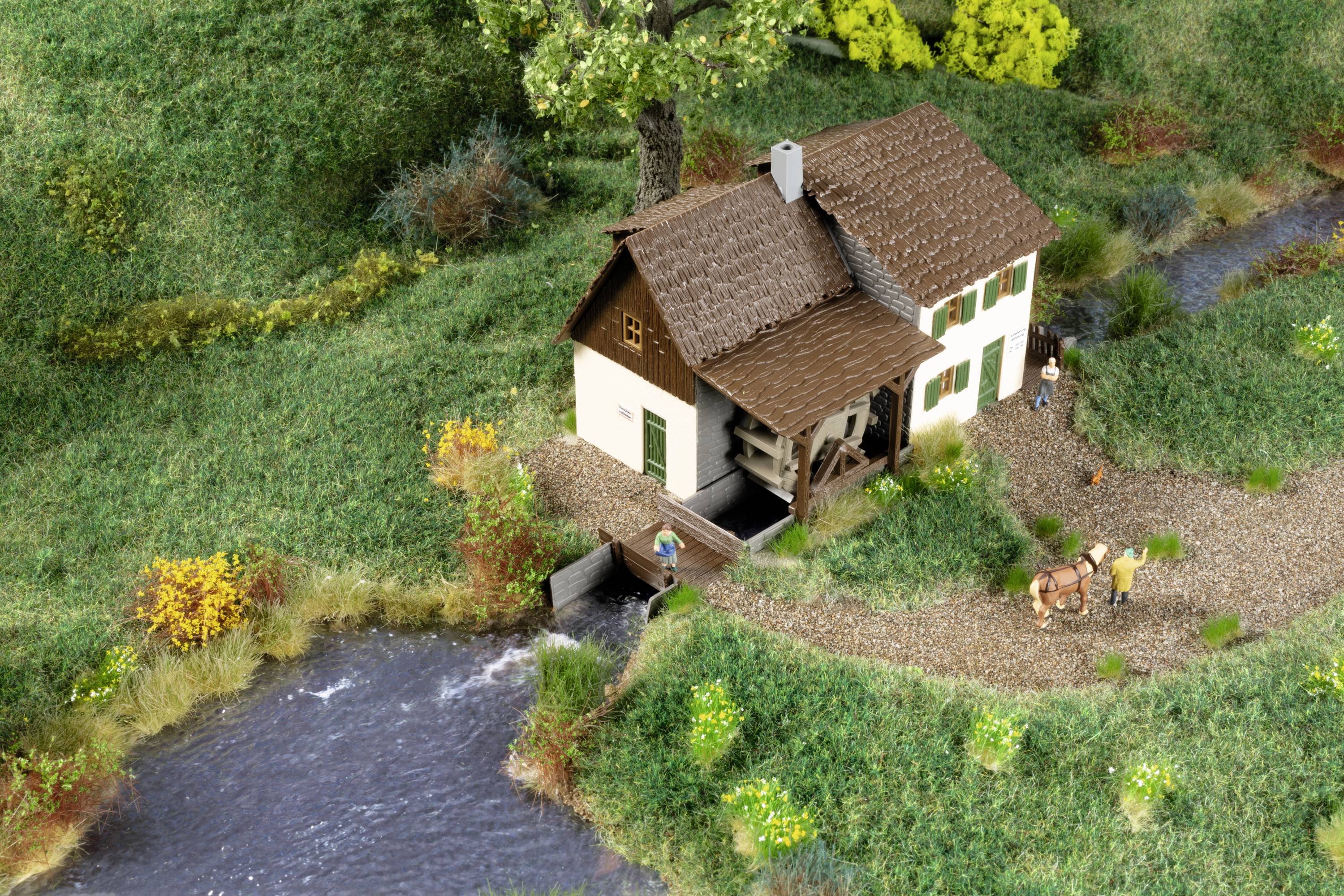 Ein Miniaturmodell eines ländlichen Hauses mit Personen, einem Pferd und Bach in einer grünen Landschaft.