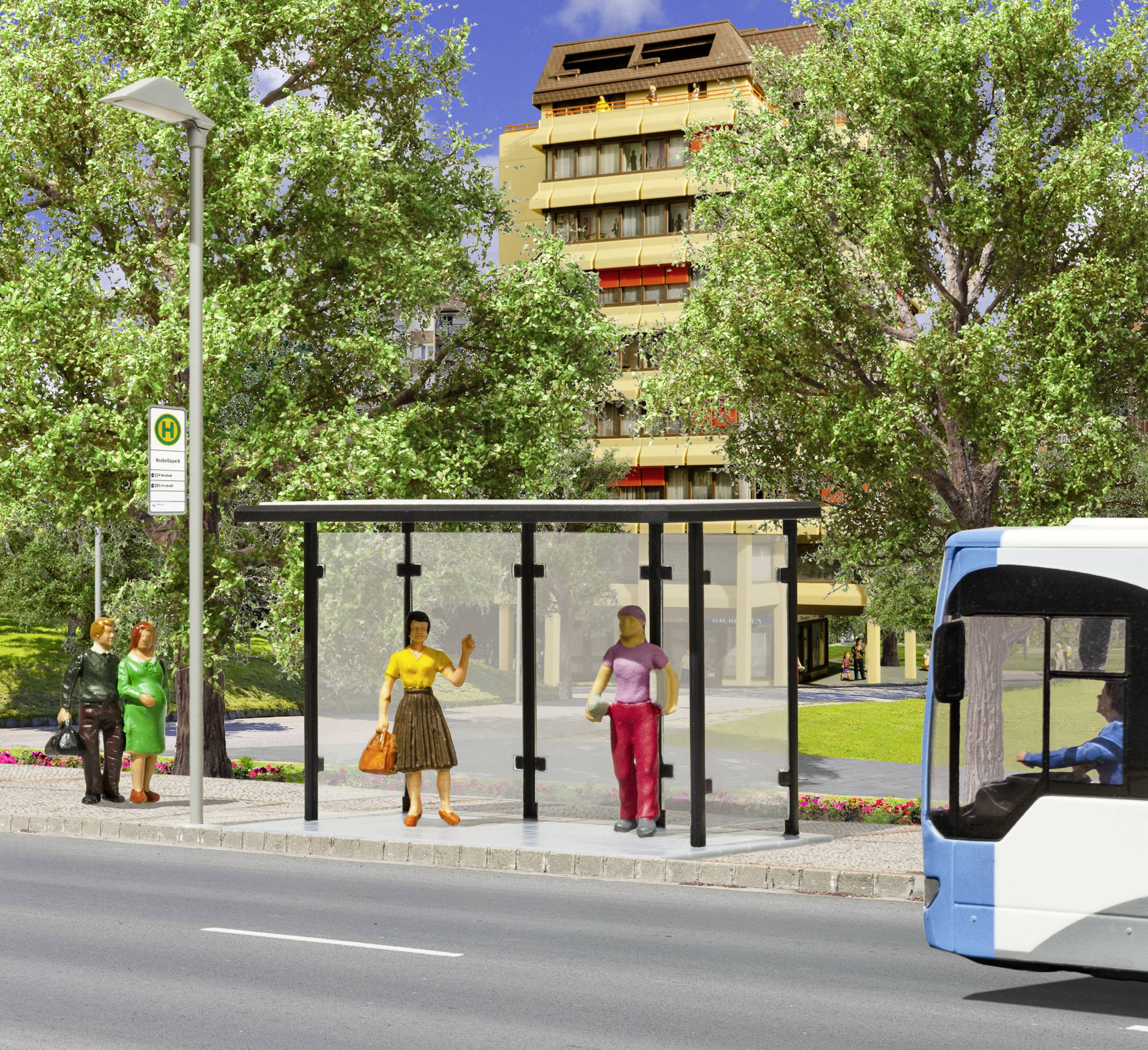 Bushaltestelle mit wartenden Personen, einem vorbeifahrenden Bus und einem Wohngebäude im Hintergrund. Bäume säumen die Straße.