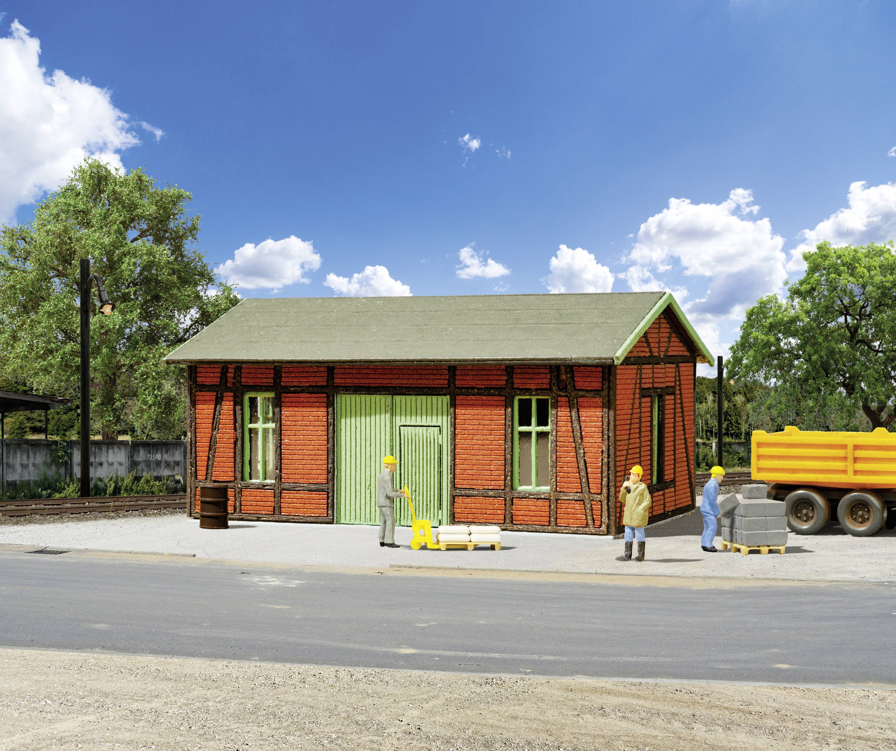 Altes, rotes Backsteinlagerhaus mit grünem Holztor. Drei Bauarbeiter tragen Sicherheitshelme. Ein orangefarbener Lastwagen steht neben Paletten.