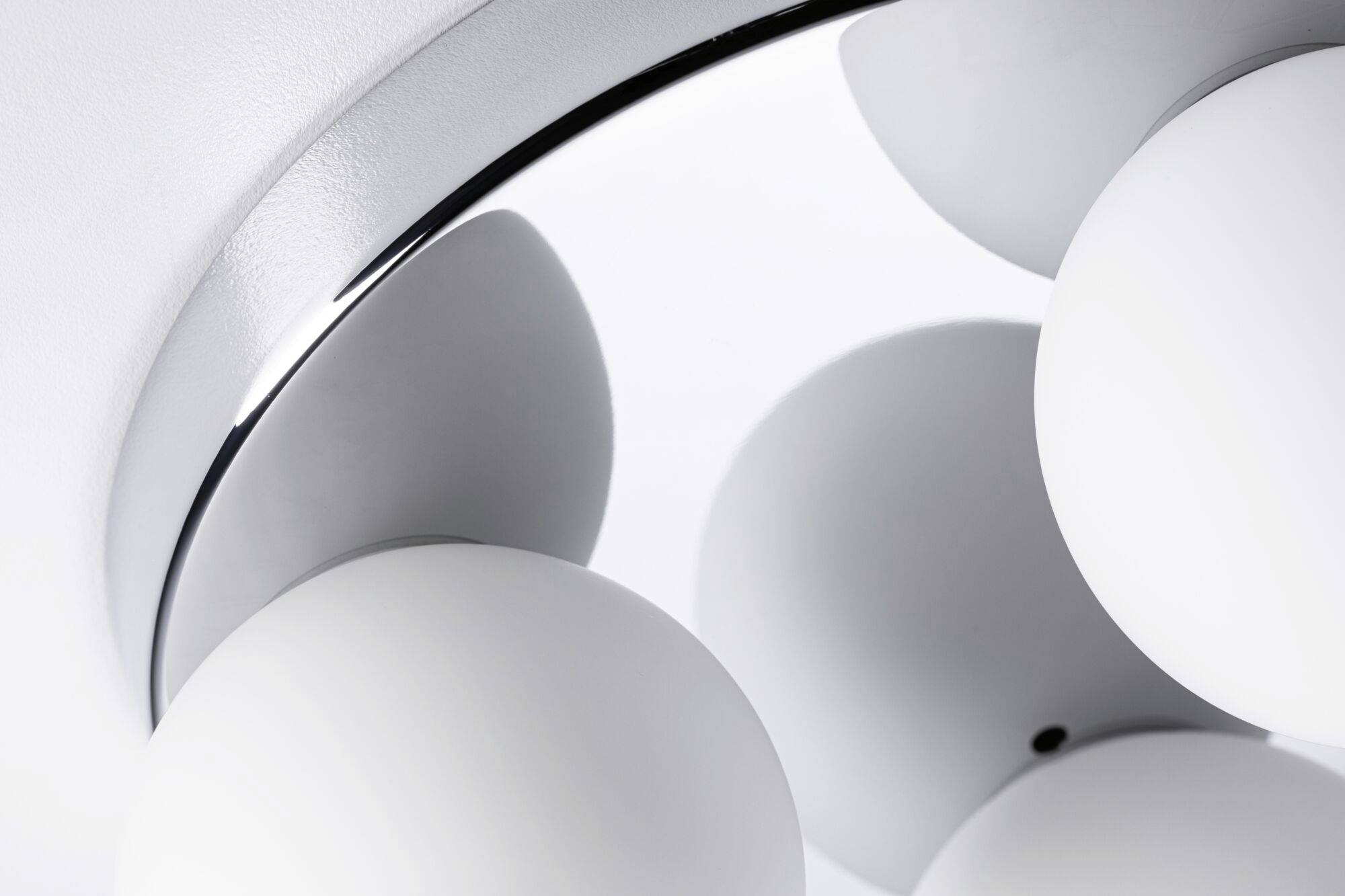 Nahaufnahme einer modernen Deckenleuchte mit kugelförmigen, weißen Glaslampen, die an einer metallischen Halterung befestigt sind.