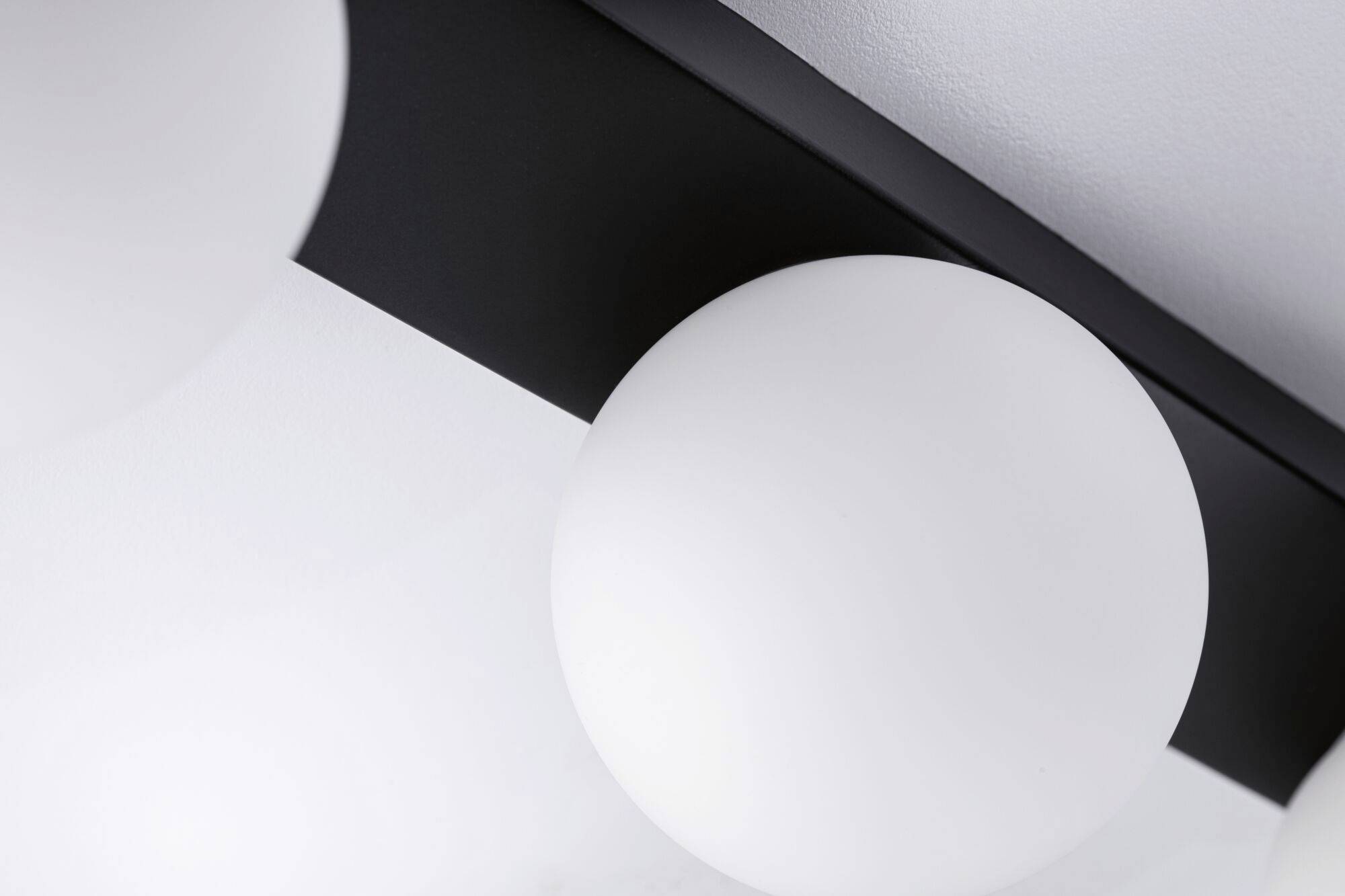 Eine moderne Deckenleuchte mit kugelförmigem, weißem Lampenschirm und schwarzer Halterung vor einem weißen Hintergrund.