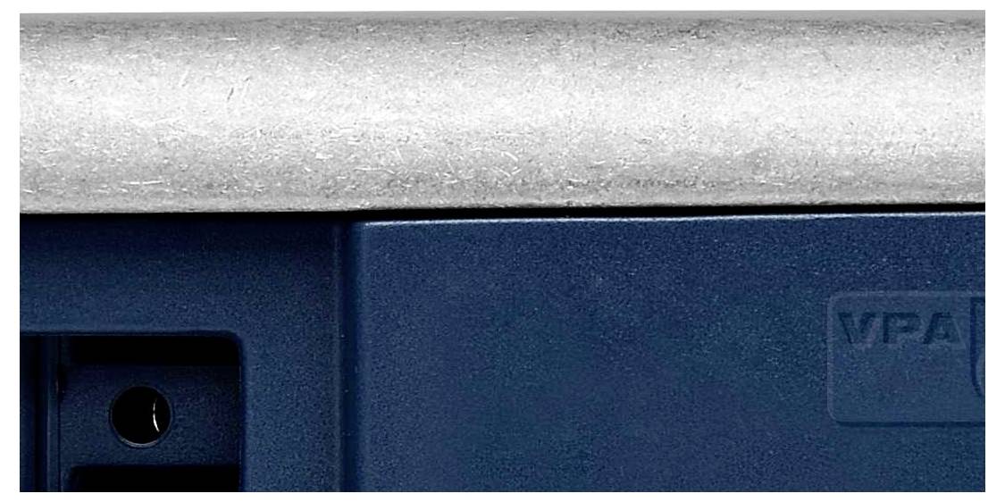 Ein Teil eines blauen Gerätes mit einer metallischen Oberfläche sichtbar, ein kleiner Ausschnitt eines elektronischen Anschlusses ist zu sehen.